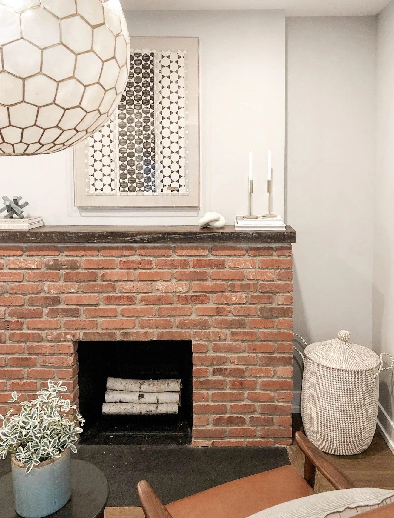 Close up of capiz shell globe pendant light hanging above a brick fireplace with framed artwork and decorative accents.