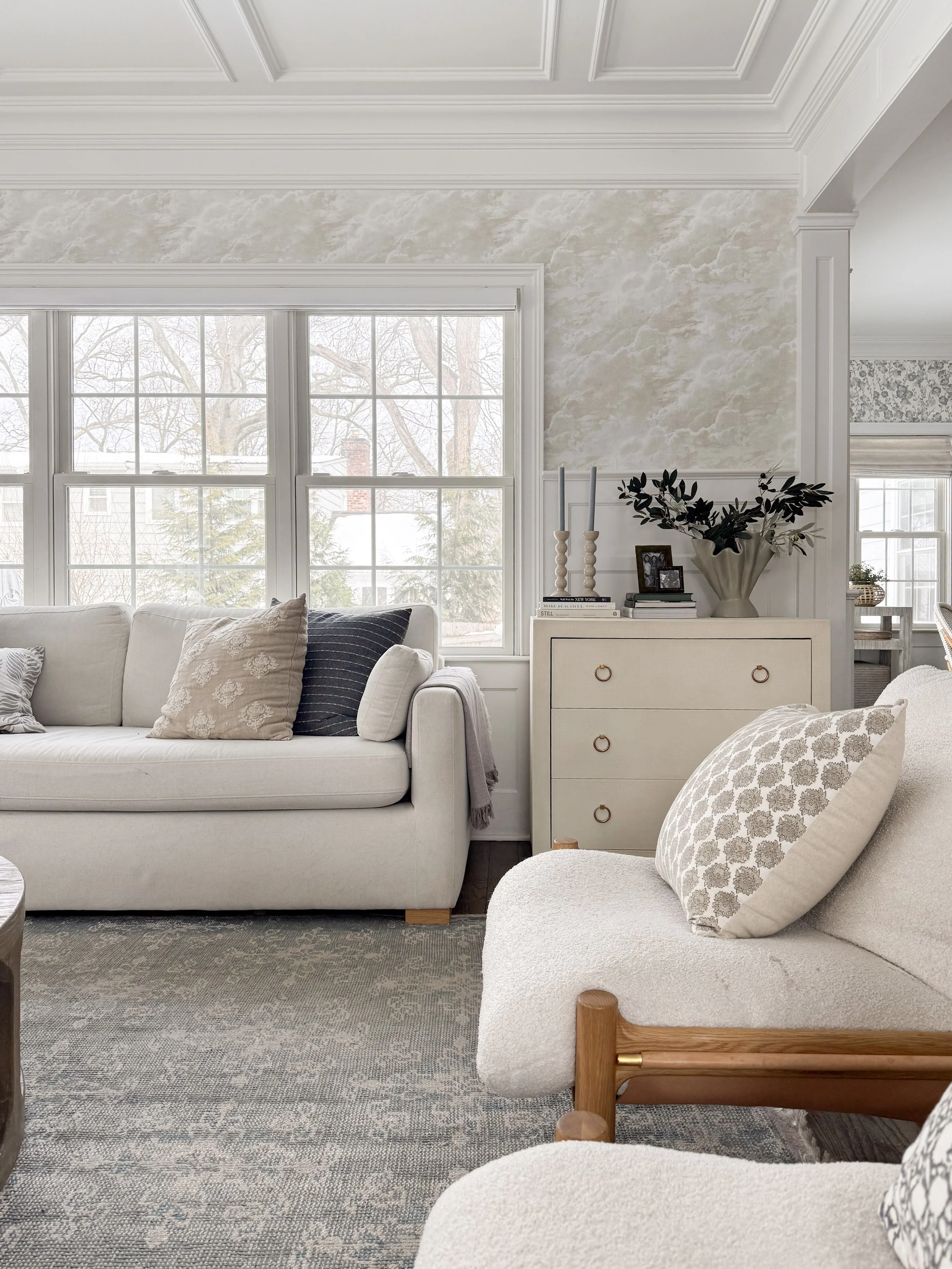Light filled living room with spoonflower cloud wallpaper, coffered ceiling, white trim, and neutral furniture creating a bright coastal inspired space.