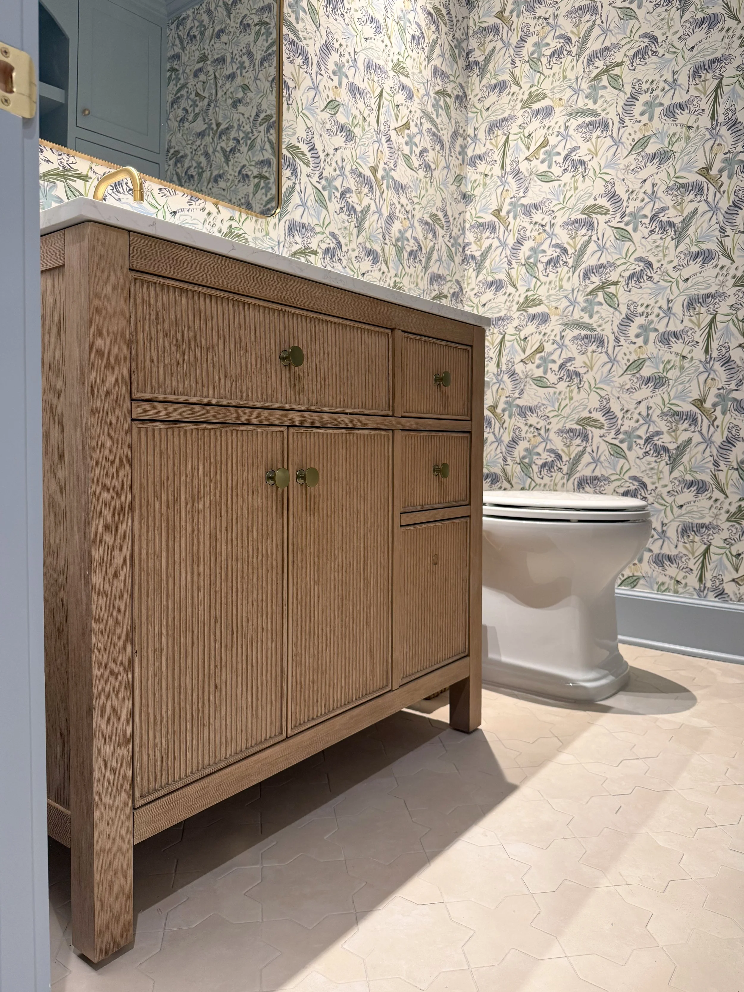 Birch Lane reeded wood vanity with marble countertop and brass hardware against blue tiger wallpaper.