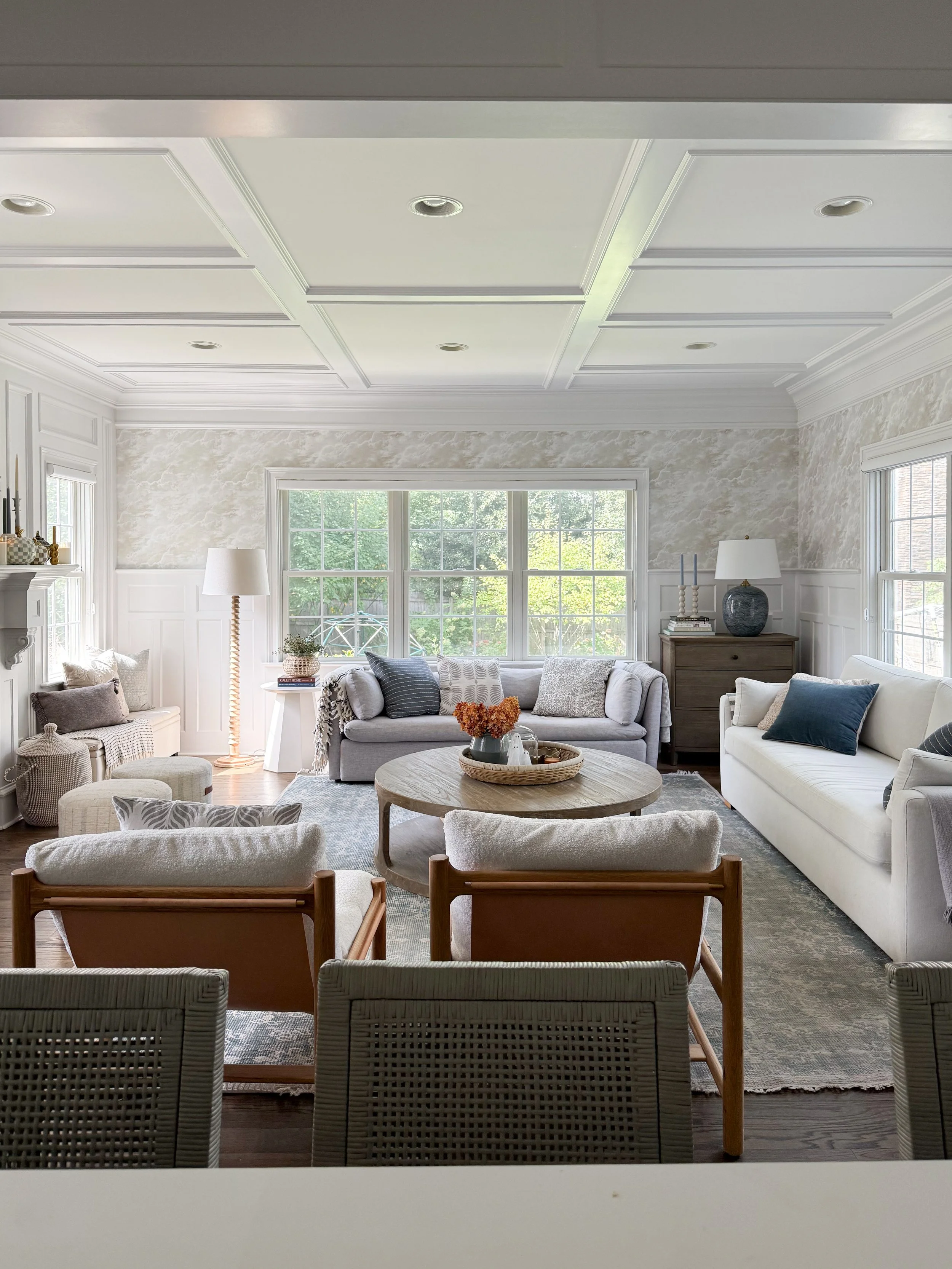 Bright neutral living room styled for fall with layered seating, warm wood accents, textured pillows, dried hydrangeas, and subtle organic fall decor.