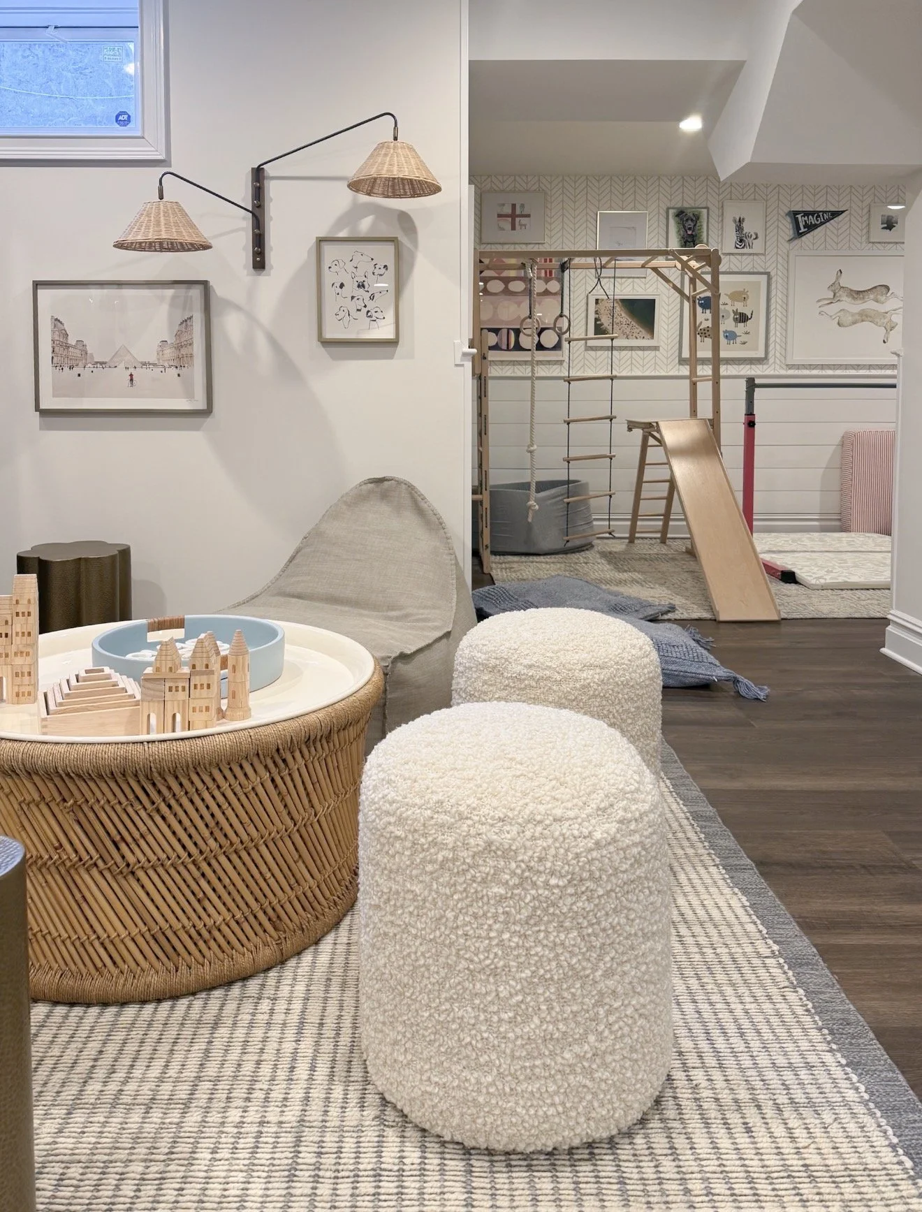 Neutral kids playroom with soft rugs, woven play table, climbing structure, and light paint colors creating a calm family play space.