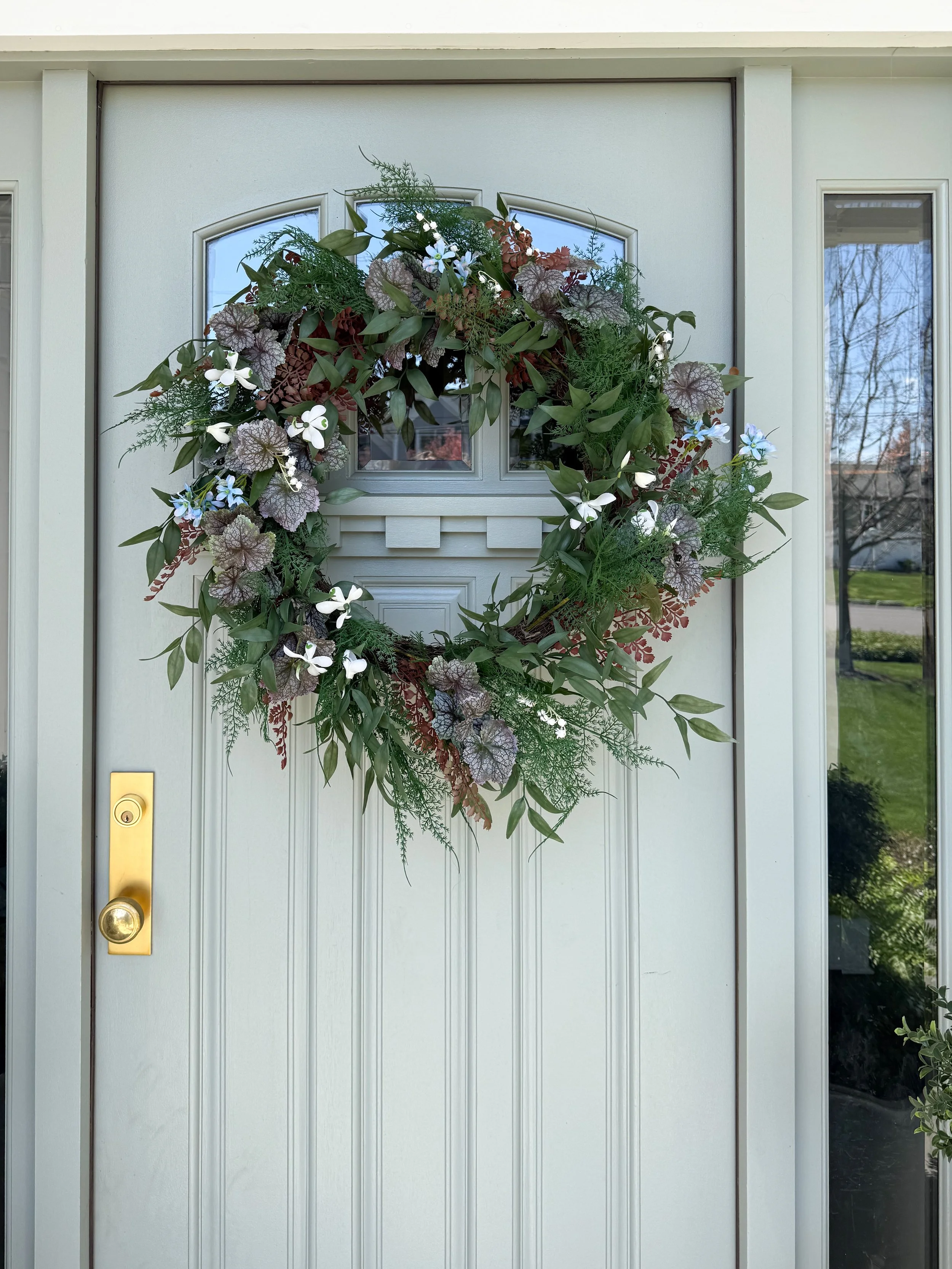 Close up of elegant spring wreath with mixed greenery, white flowers, and natural textures on front door