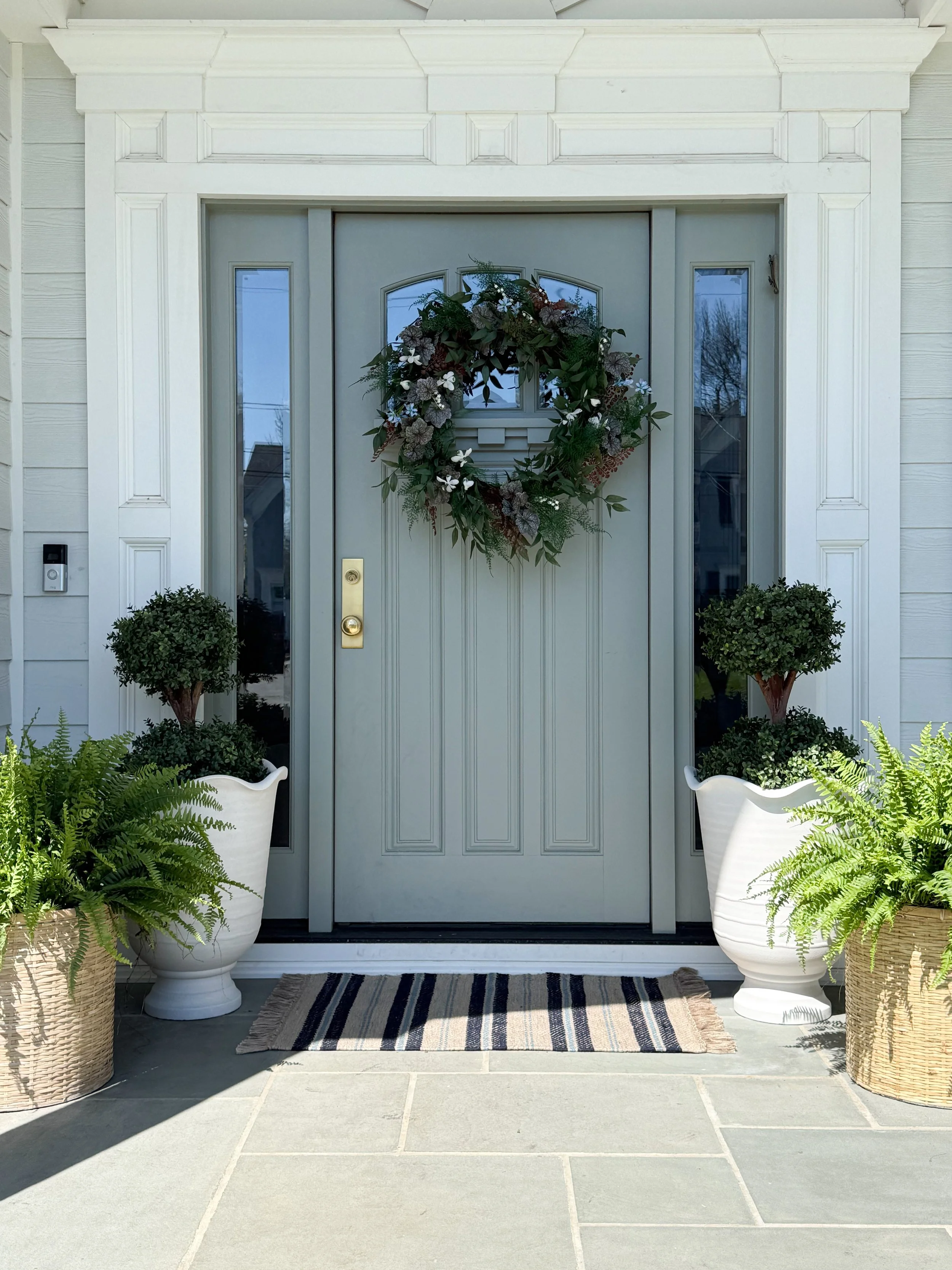 Neutral green front door with gold hardware and asymmetrical spring wreath with greenery and white florals