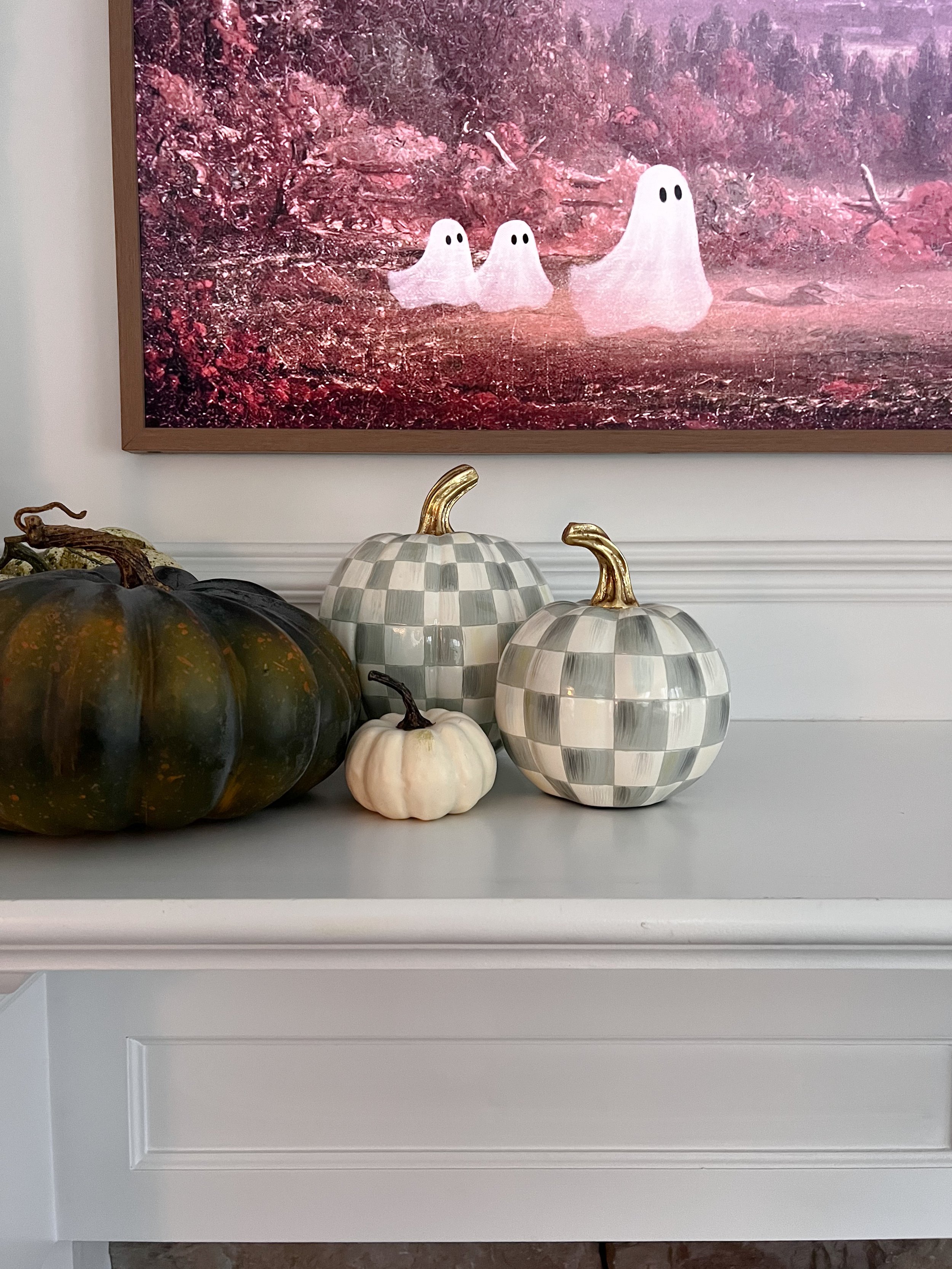 Fall mantel decor with green and white checkered pumpkins, natural pumpkins, and whimsical ghost artwork for a playful seasonal living room.