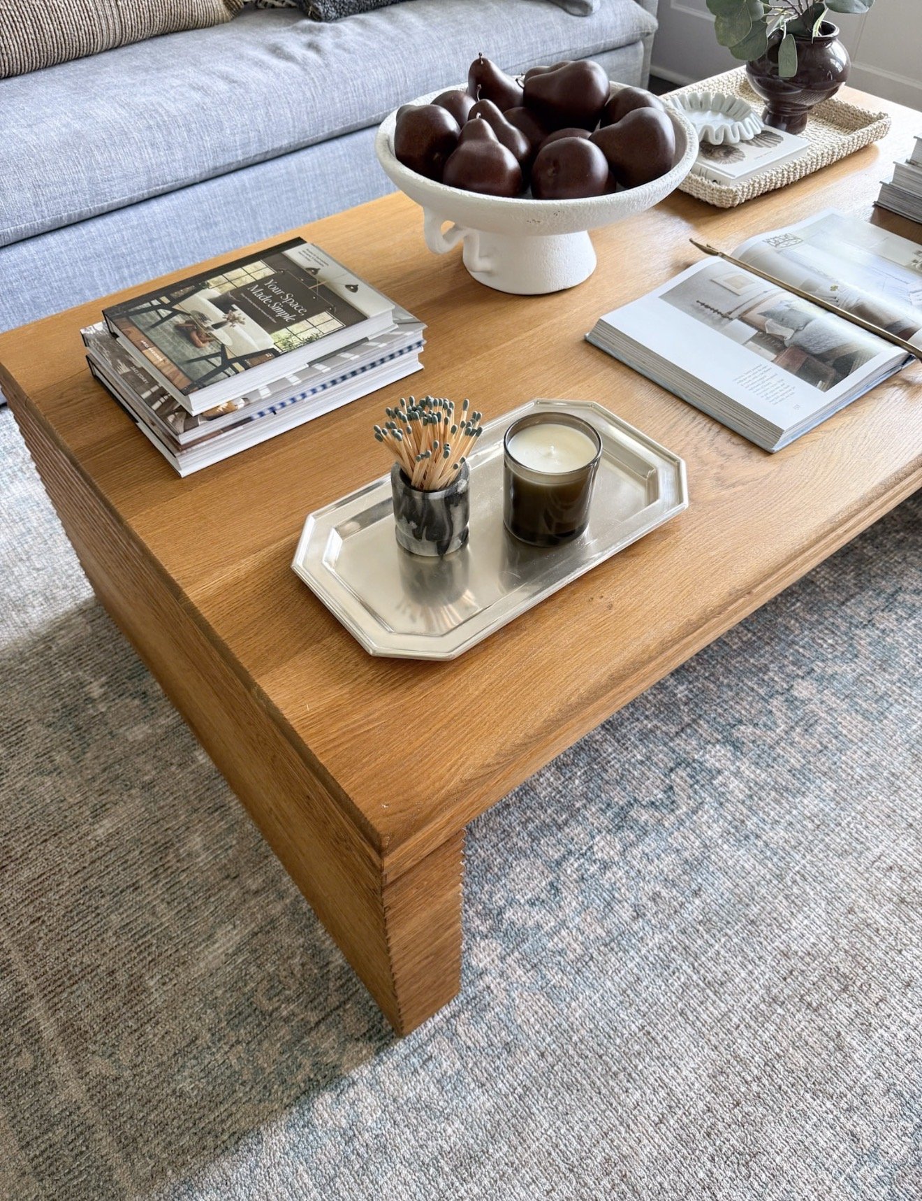 Warm wood coffee table styled with books, a candle, decorative bowl, and accessories over a muted blue and neutral Loloi area rug.