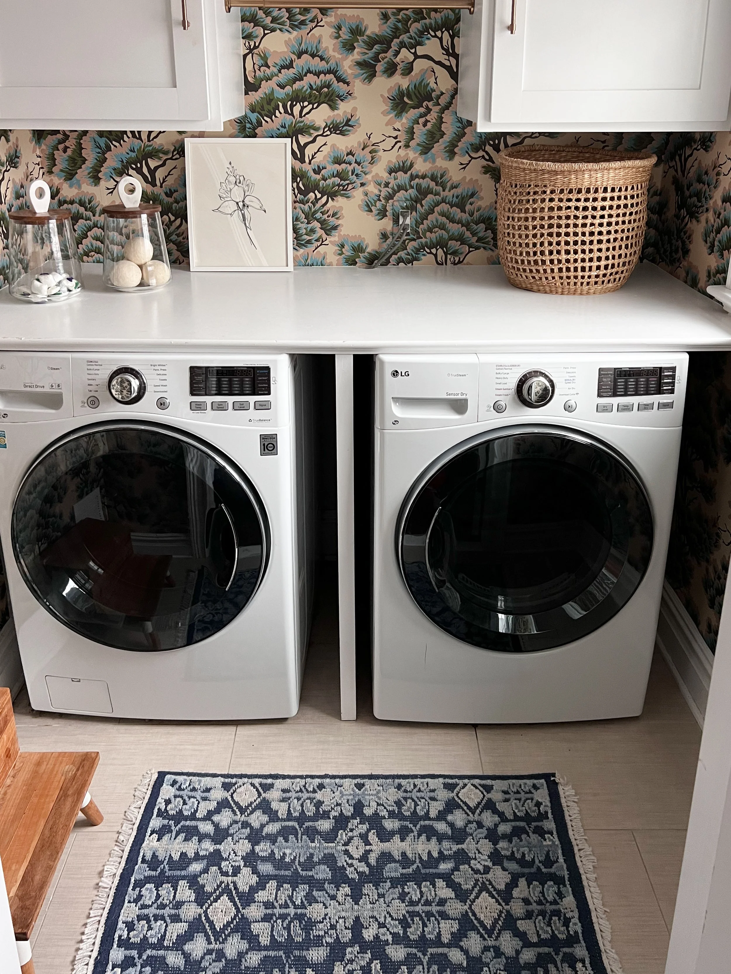 Stylish laundry room with floral wallpaper, custom cabinetry, and a blue vintage inspired runner rug.