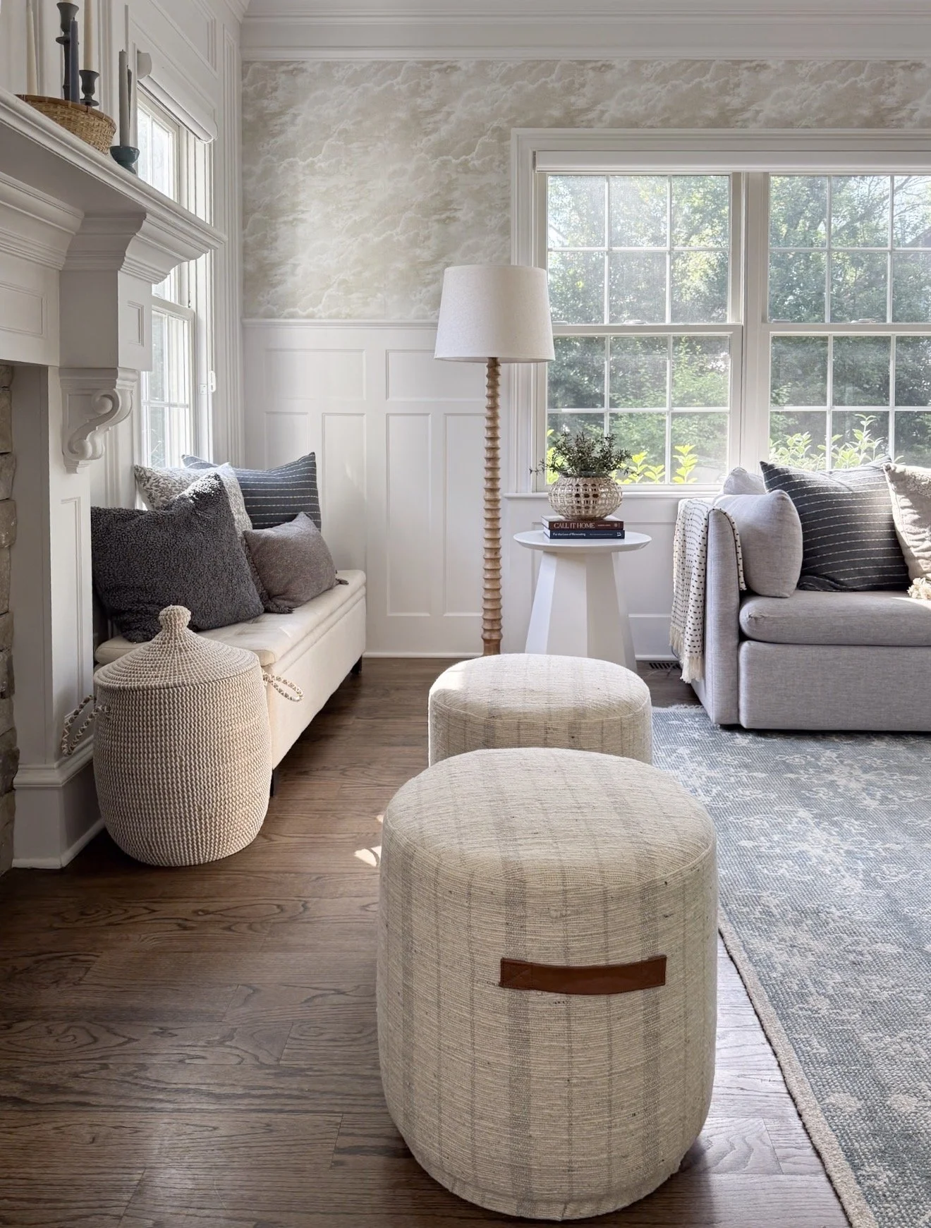 Two neutral McGee & Co McKay ottomans in front of sofa with gray and patterned pillows, showing textured woven design and cozy living room styling with natural light.