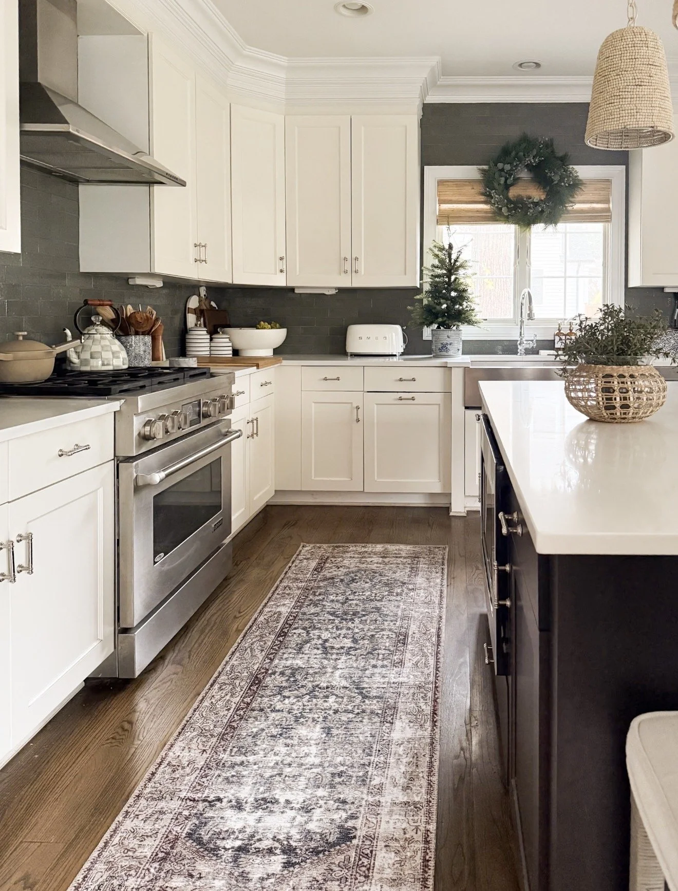 White kitchen with dark wood floors, stainless steel range, woven pendant lights, and a vintage-style Loloi runner in muted neutral tones.