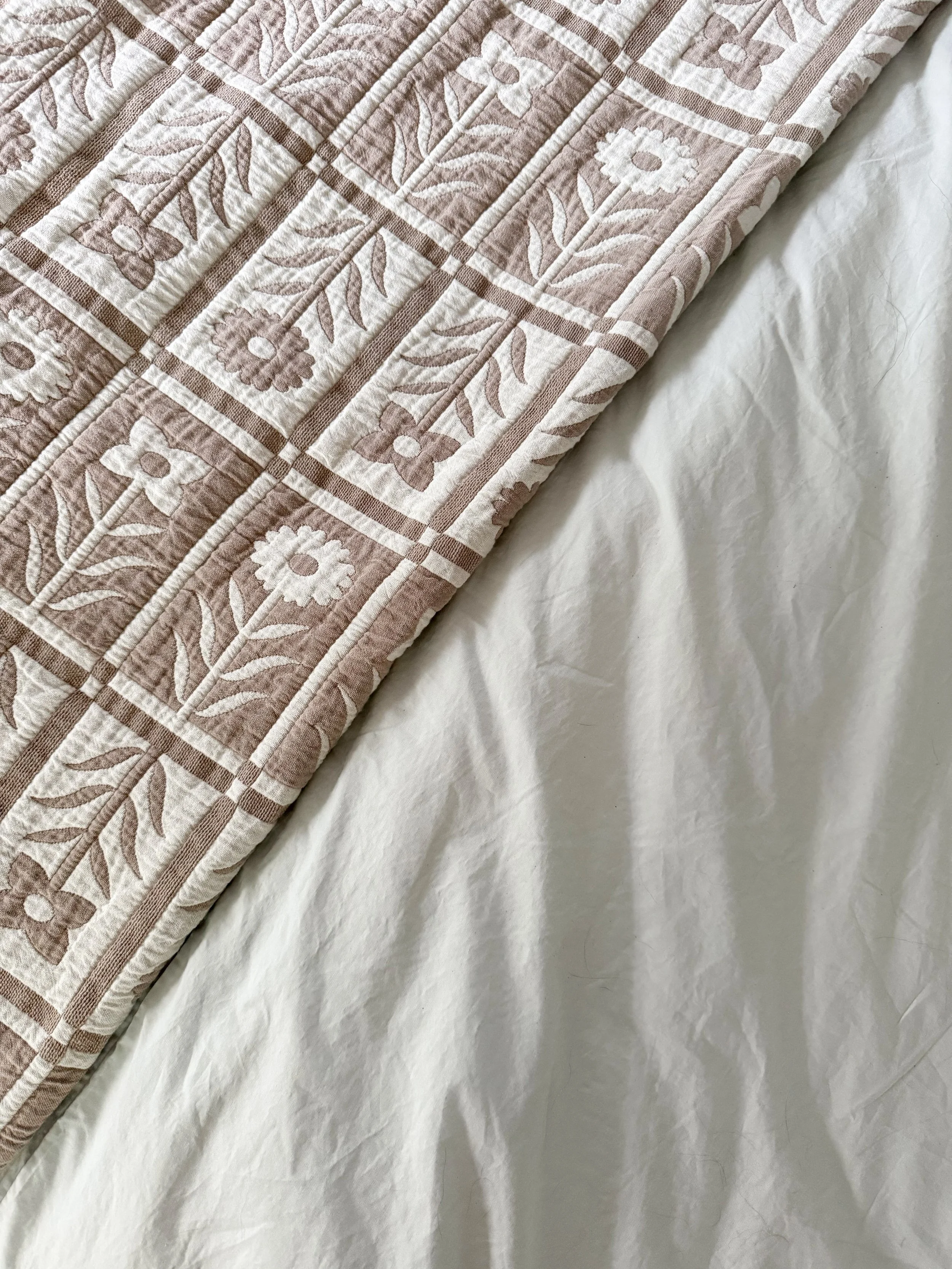 Detailed view of Quince floral quilt layered over soft white linen bedding, showcasing texture and quality craftsmanship.