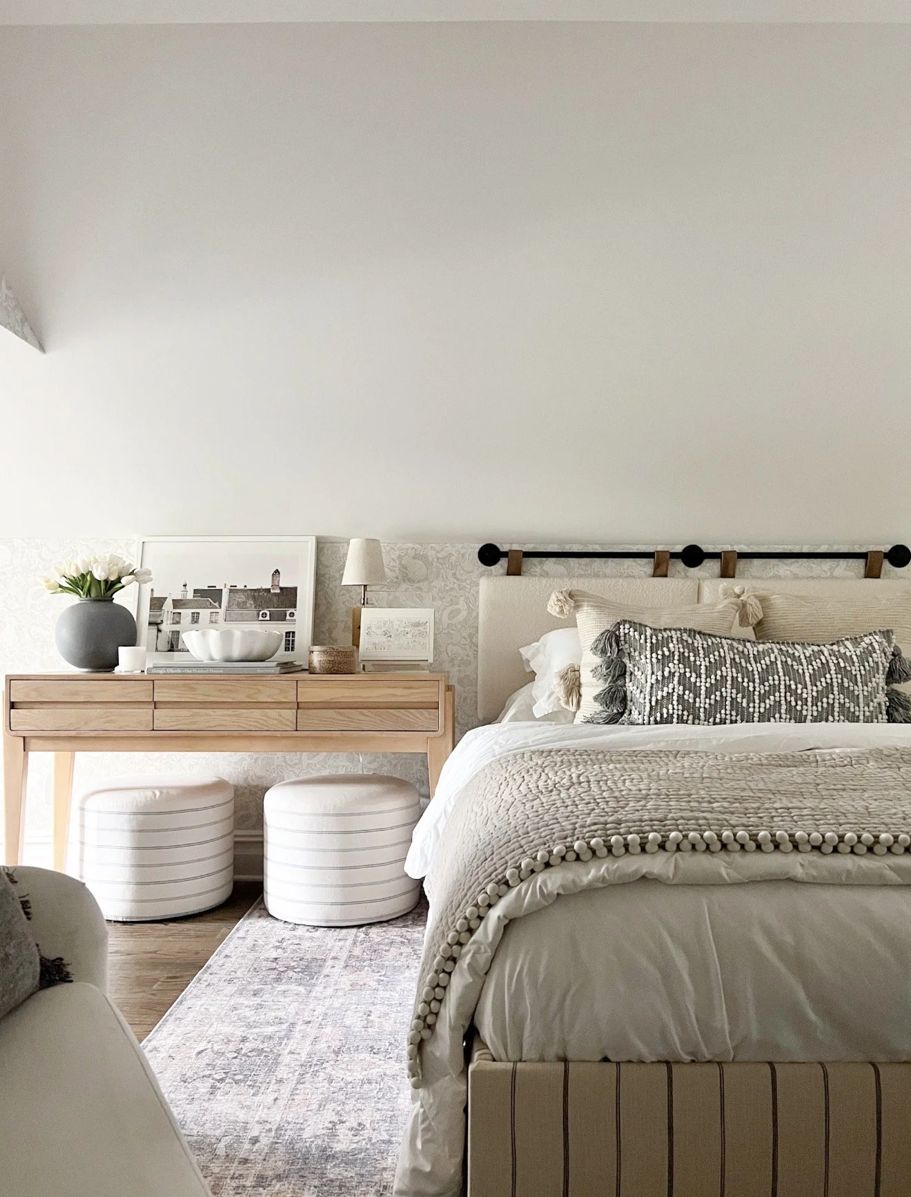 Primary bedroom with Sherwin Williams Aesthetic White walls, upholstered bed, neutral bedding, wood console table, and soft layered textures.