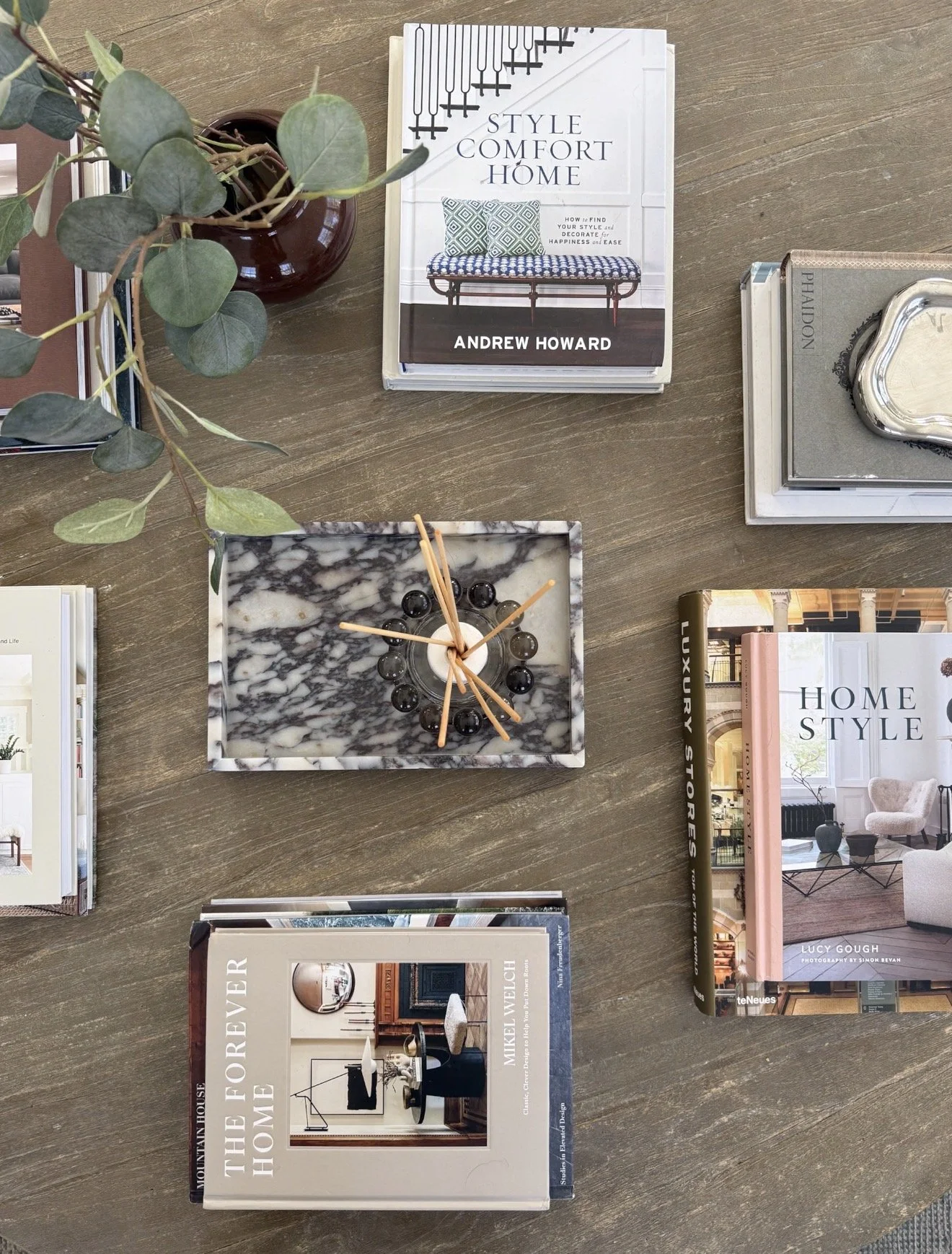Neutral coffee table books layered with marble decor, eucalyptus stems, and decorative accessories for elevated coastal traditional home styling