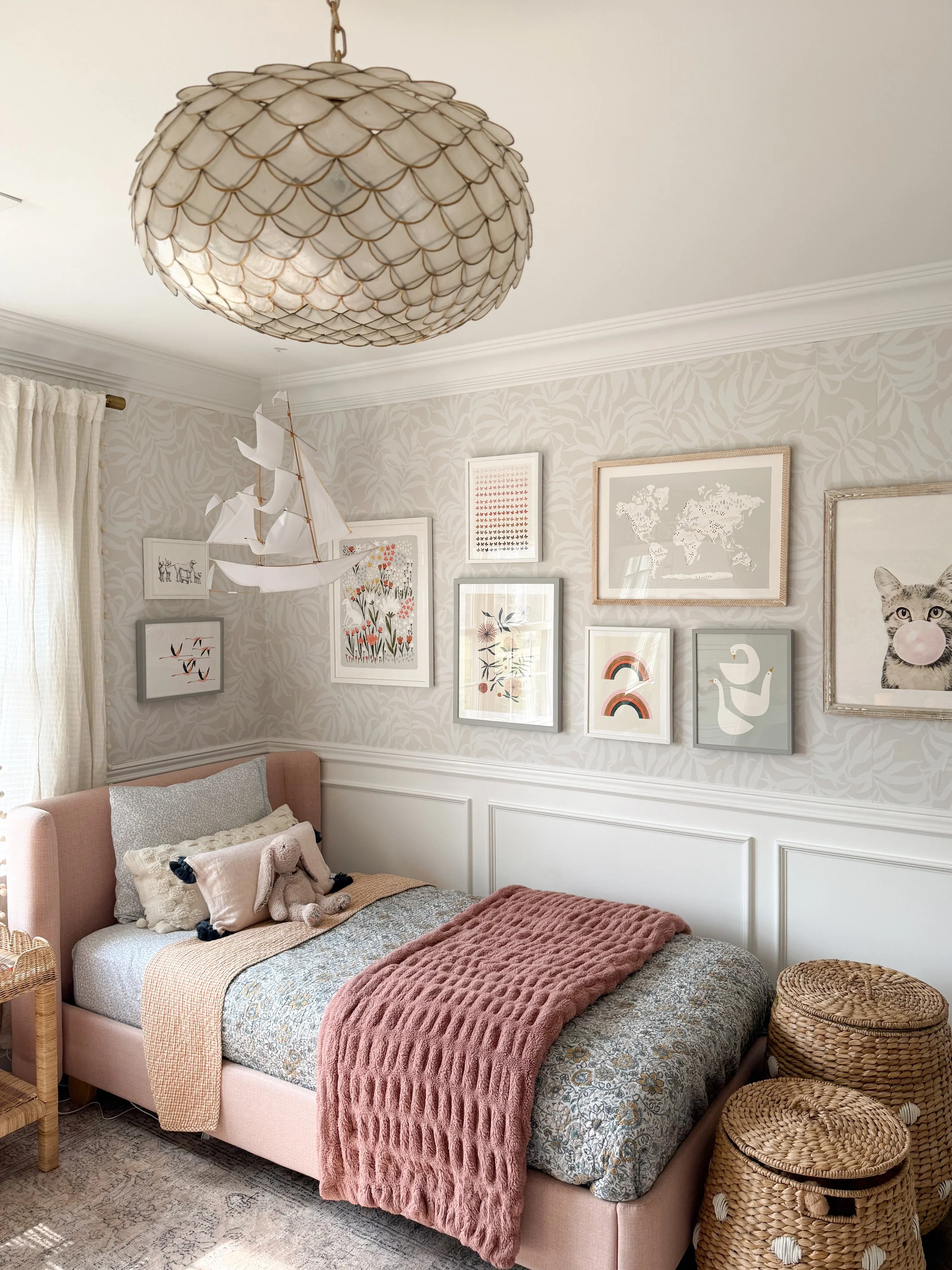 Girls bedroom with a shell chandelier, blush upholstered bed, wallpaper, and layered children's room decor.