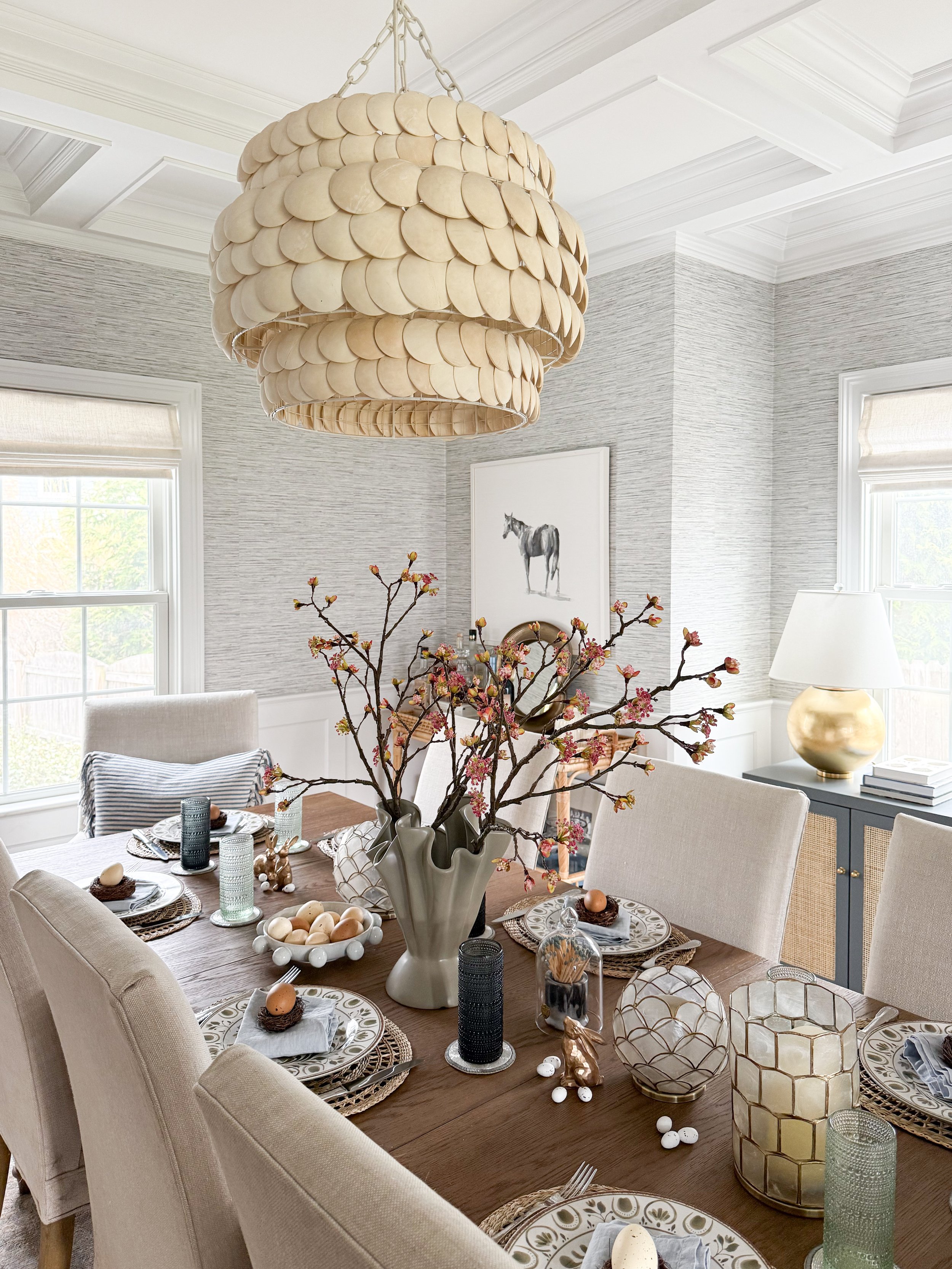 Spring tablescape centerpiece with sculptural ceramic vase, blooming branches, and layered place settings with patterned plates and linen napkins