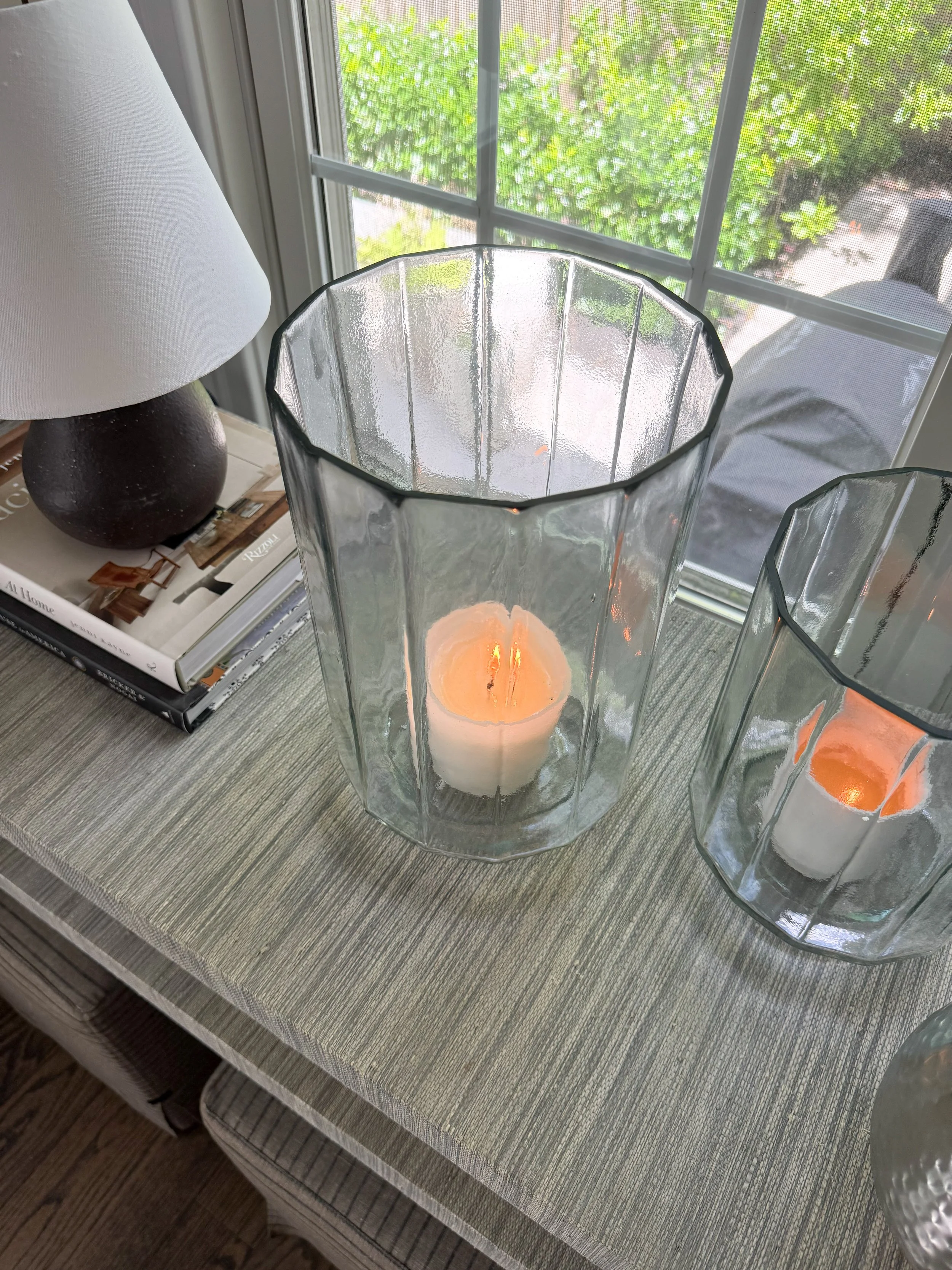 Glass hurricane candle holders with pillar candles styled on a dining room console table alongside decorative accessories for classic McGee & Co home decor.