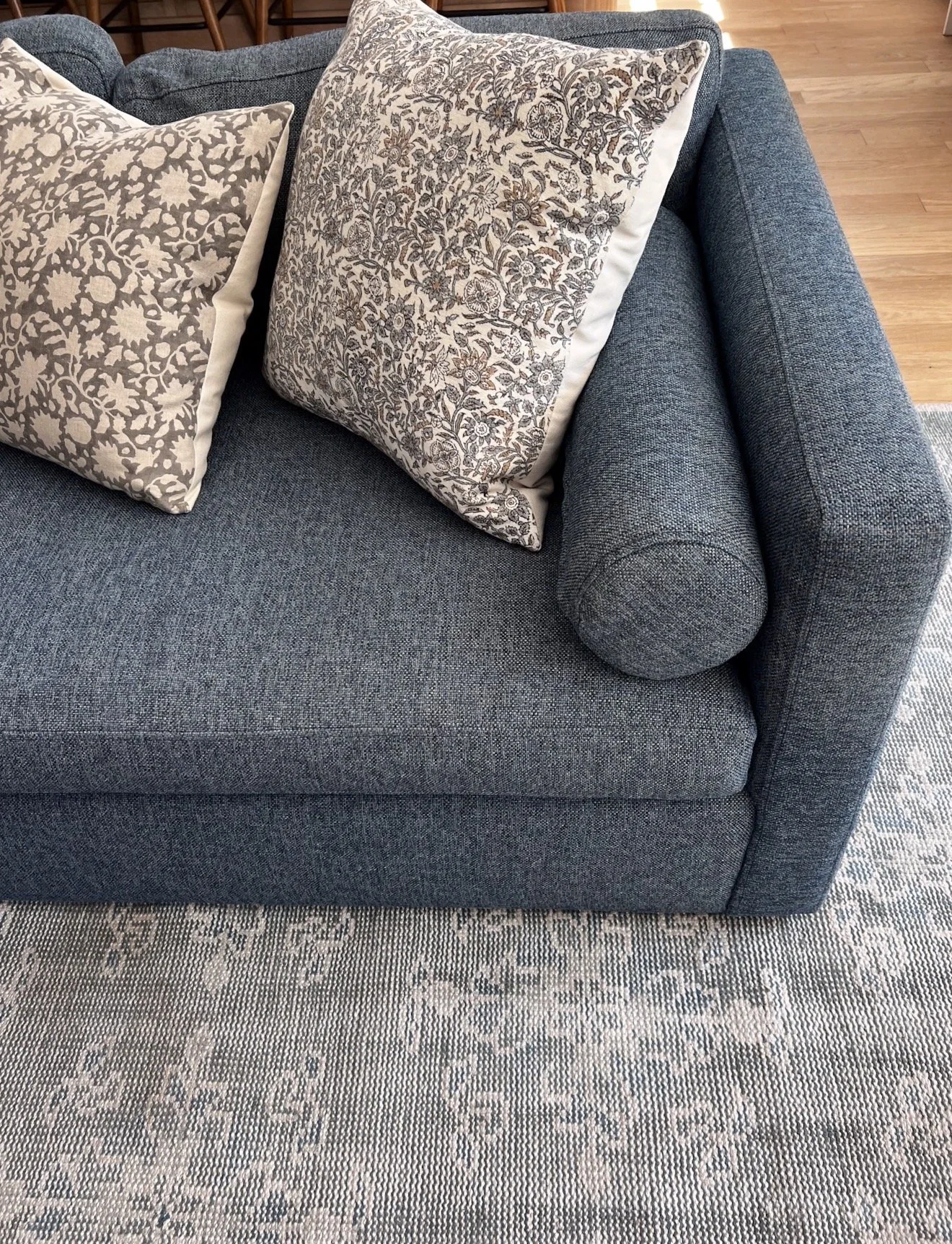 Bright living room with a blue sectional, patterned throw pillows, blue and gray area rug, and neutral accent chairs.