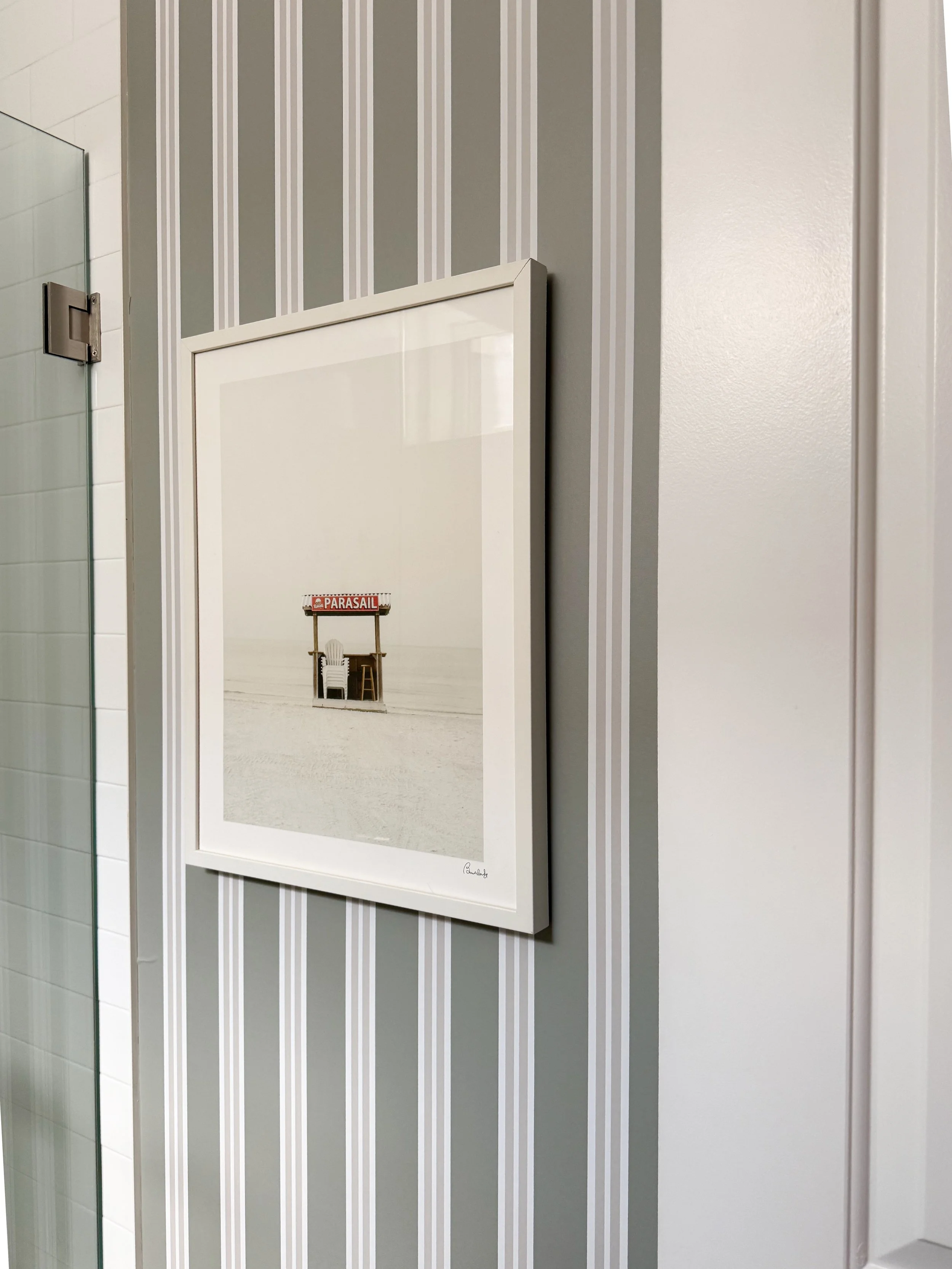 Basement bathroom accent wall featuring Chasing Paper striped wallpaper, framed beach artwork, and a minimalist neutral design with soft coastal inspired details.