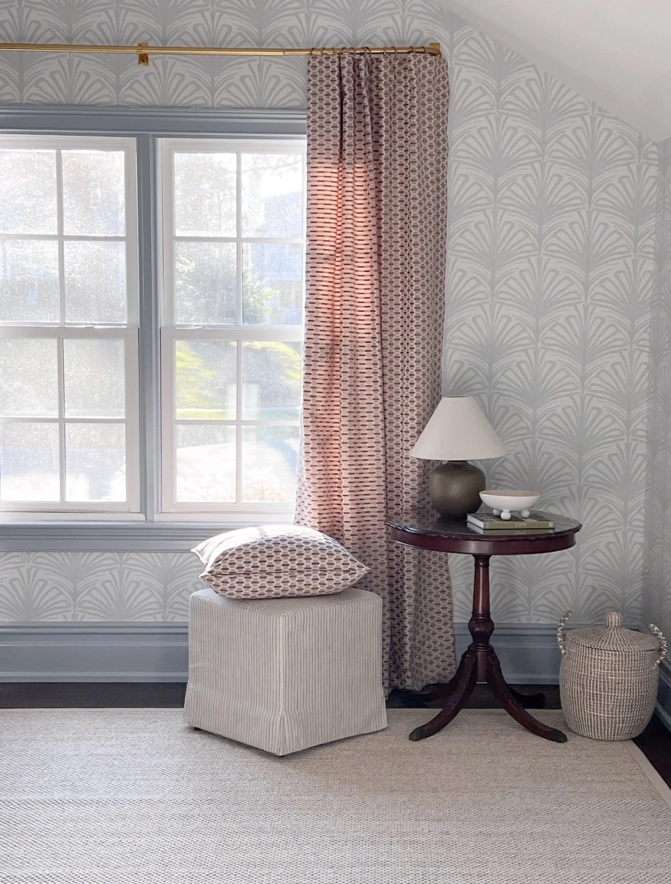 Light blue botanical wallpaper paired with a patterned rug, woven storage baskets, neutral furniture, and textured lamp shade.