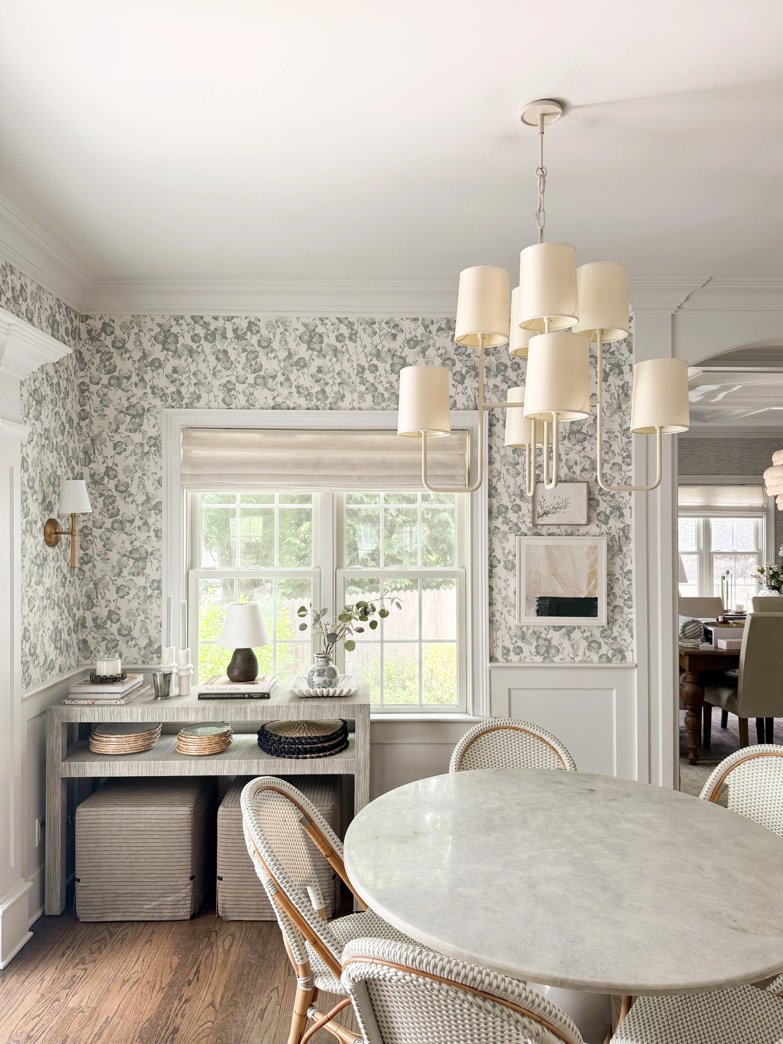 Breakfast nook featuring a modern multi-shade chandelier, floral wallpaper, and a round marble dining table.