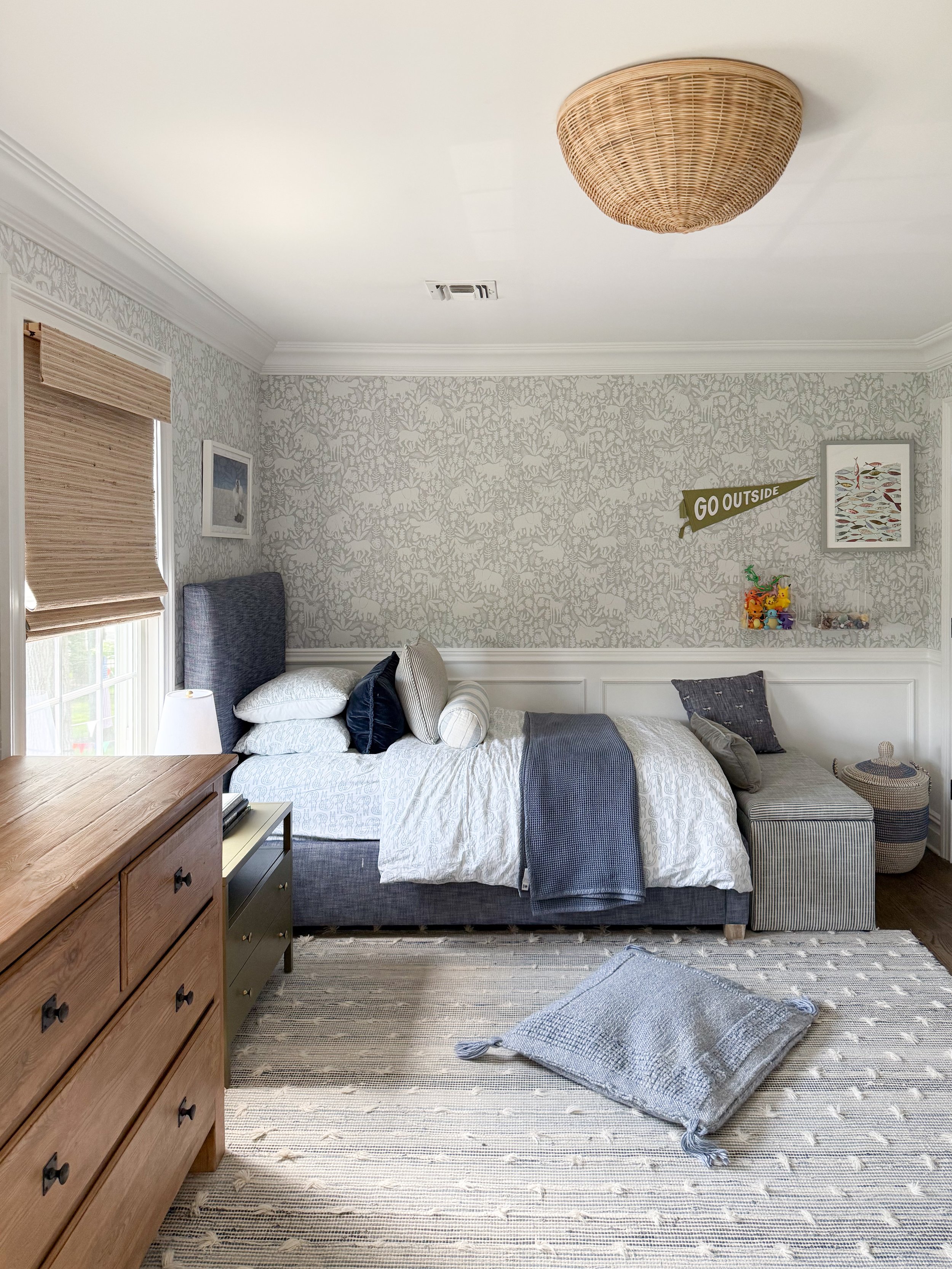 Boys bedroom with a woven flush mount ceiling light, neutral wallpaper, and layered blue and gray bedding.
