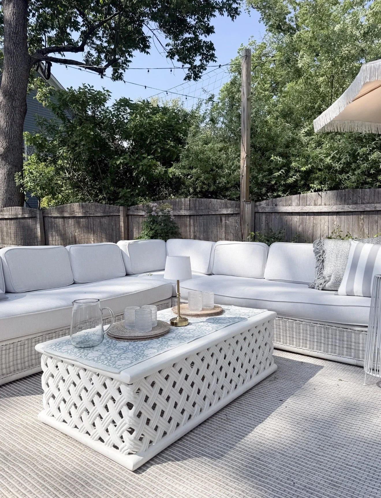 Outdoor patio lounge with a white sectional, woven coffee table, layered accessories, and a neutral Loloi outdoor area rug.