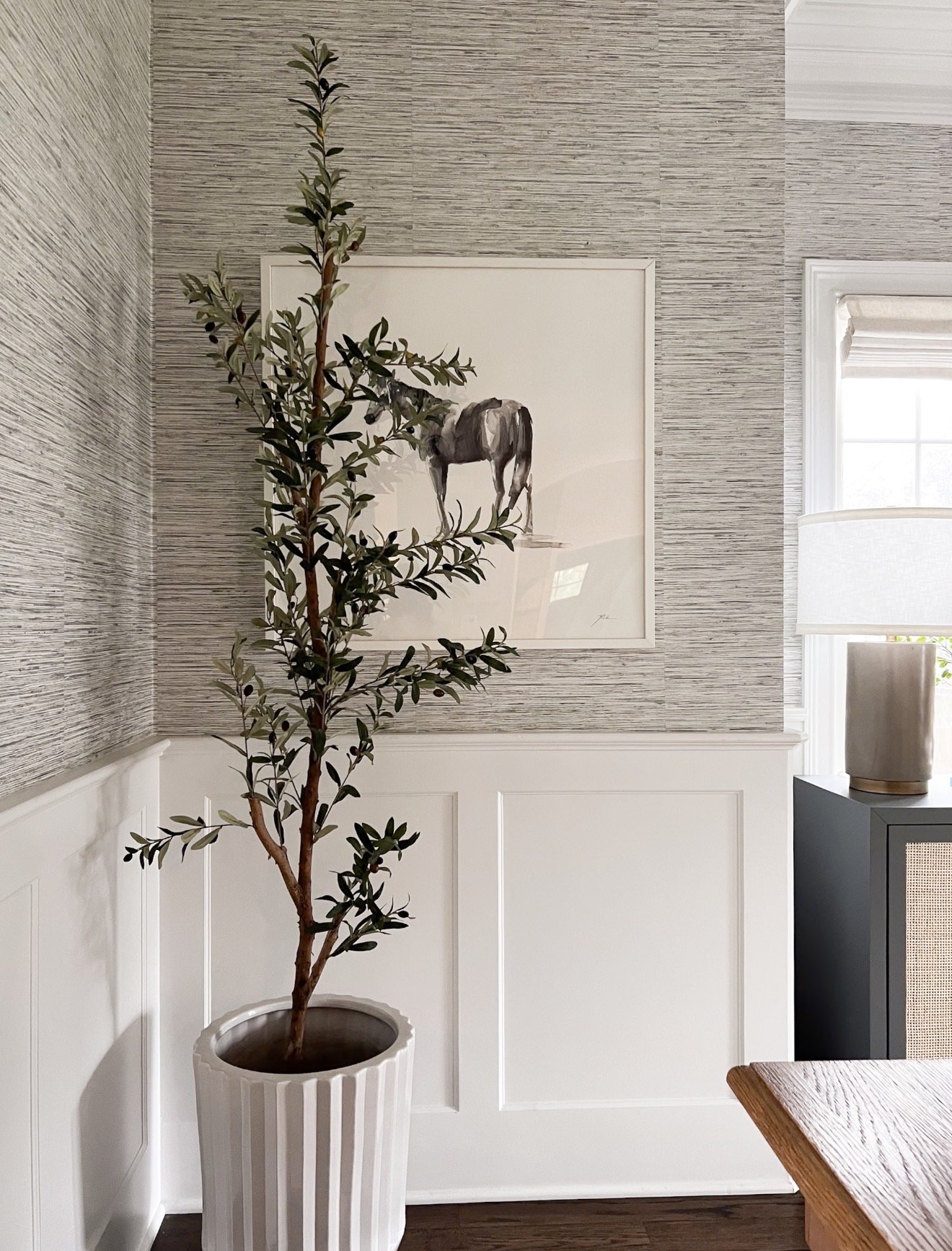 Faux olive tree in neutral planter styled beside textured wallpaper and framed horse artwork in traditional coastal inspired dining room