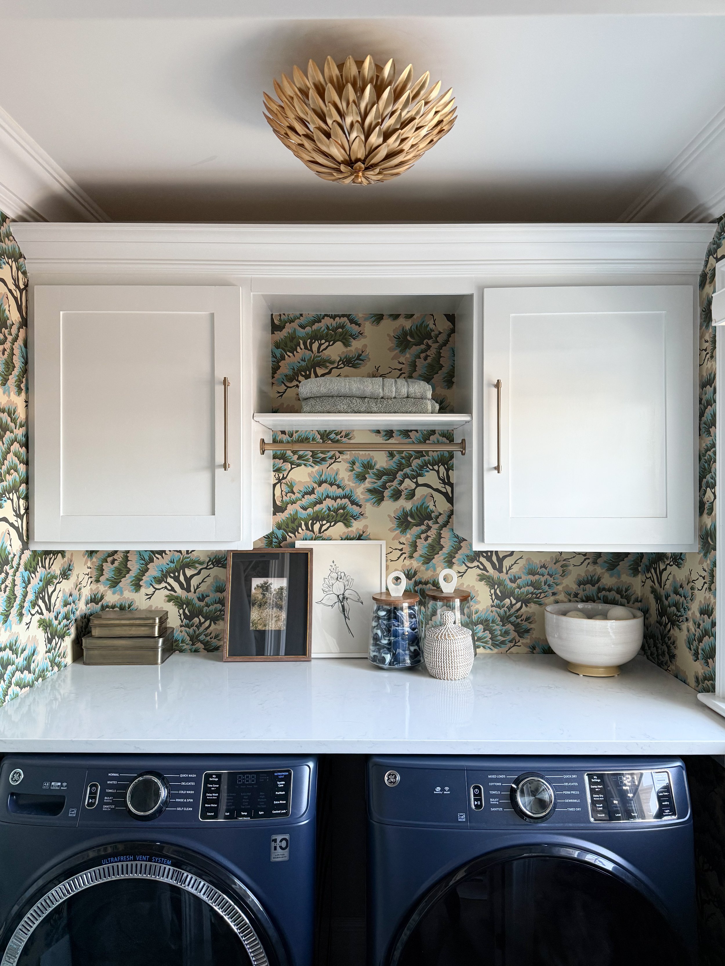 Laundry room with decorative wallpaper and a sculptural flush mount ceiling light above blue washer and dryer.