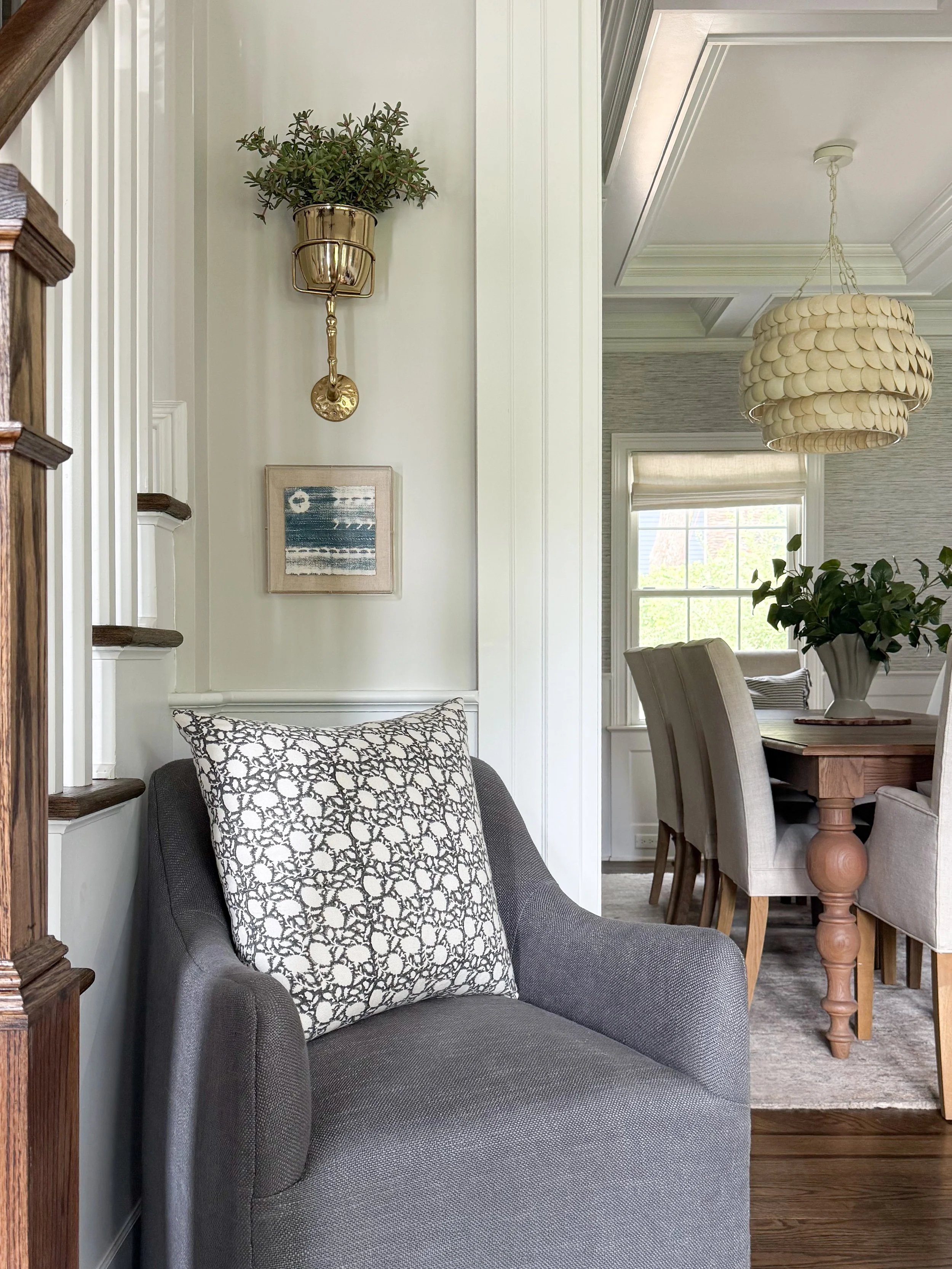 Comfortable reading corner with a neutral accent chair, wall sconce, throw pillow, and framed artwork.