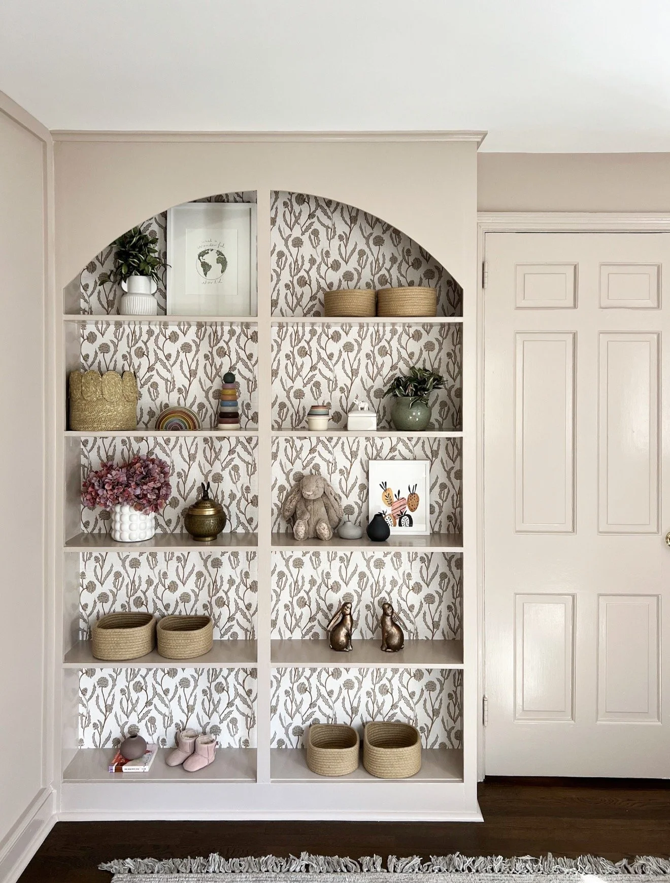 Built in shelves with neutral botanical wallpaper backing and styled kids decor accents
