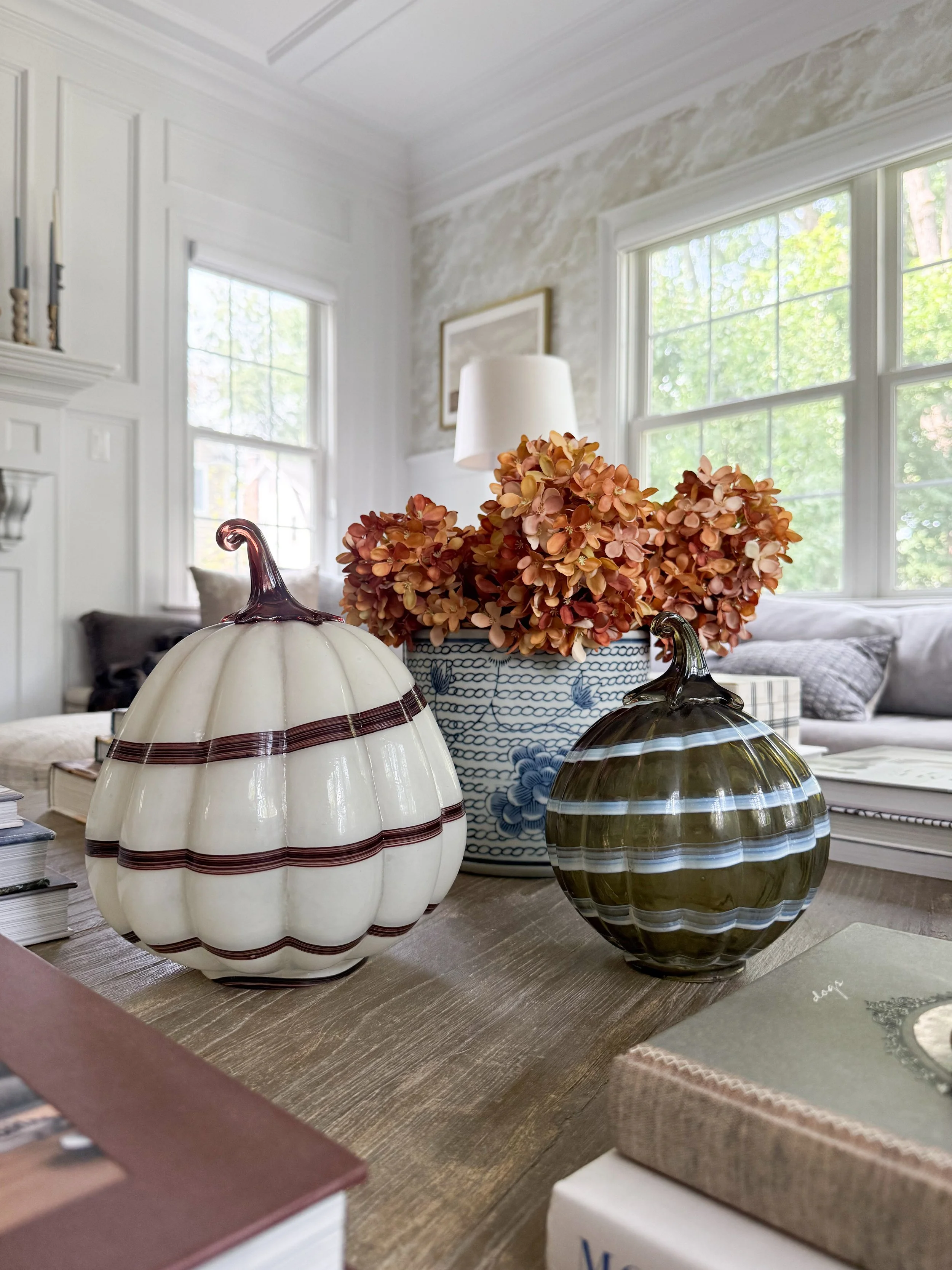 Decorative glass pumpkins in cream, burgundy, olive green, and blue styled with dried fall hydrangeas on a living room coffee table.