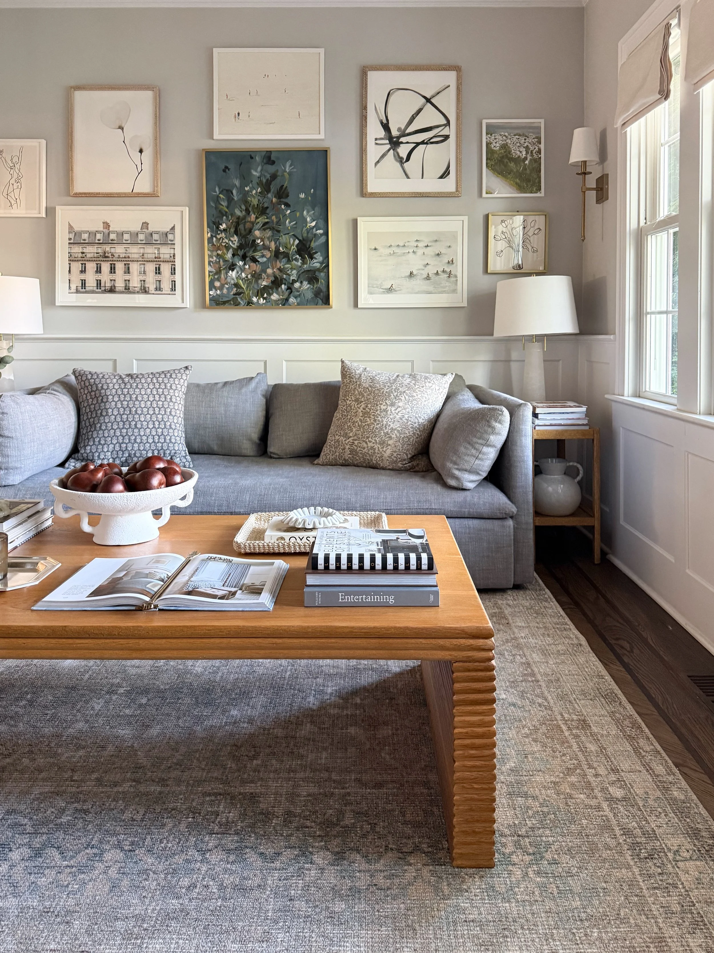 Bright transitional living room featuring a neutral sofa, vintage inspired area rug, gallery wall, layered lighting, and warm wood accents styled with Wayfair home decor.