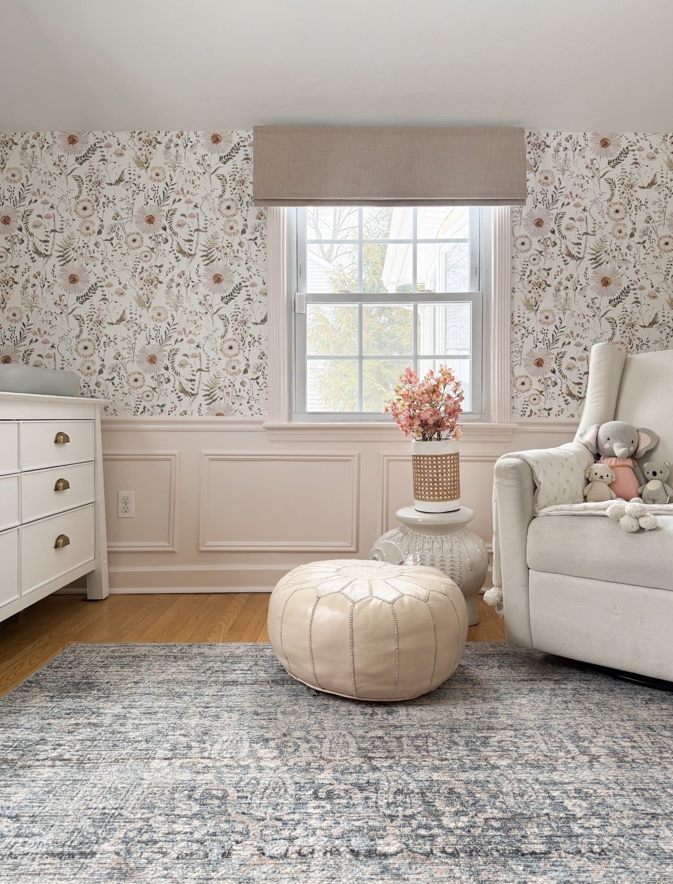 Soft neutral nursery with floral wallpaper, upholstered glider, and blush accent decor