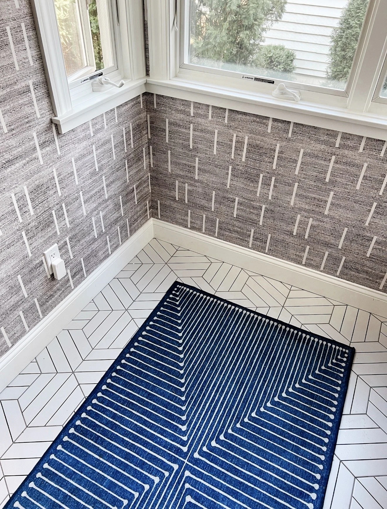 Small room with gray geometric wallpaper, white geometric tile flooring, and a blue patterned rug.