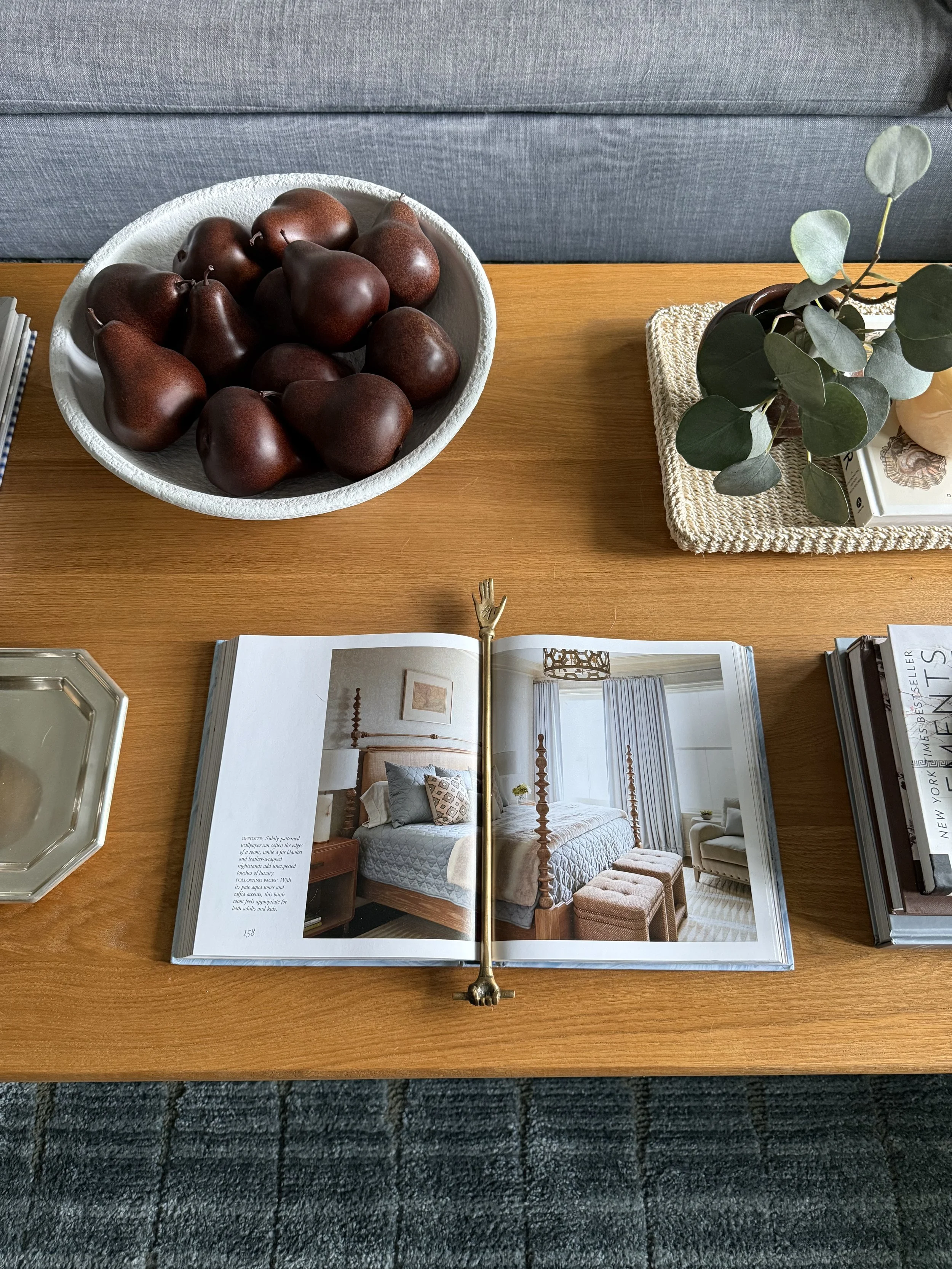 Decorative brass hand bookmark styled on open coffee table design book in cozy neutral living room with layered styling details