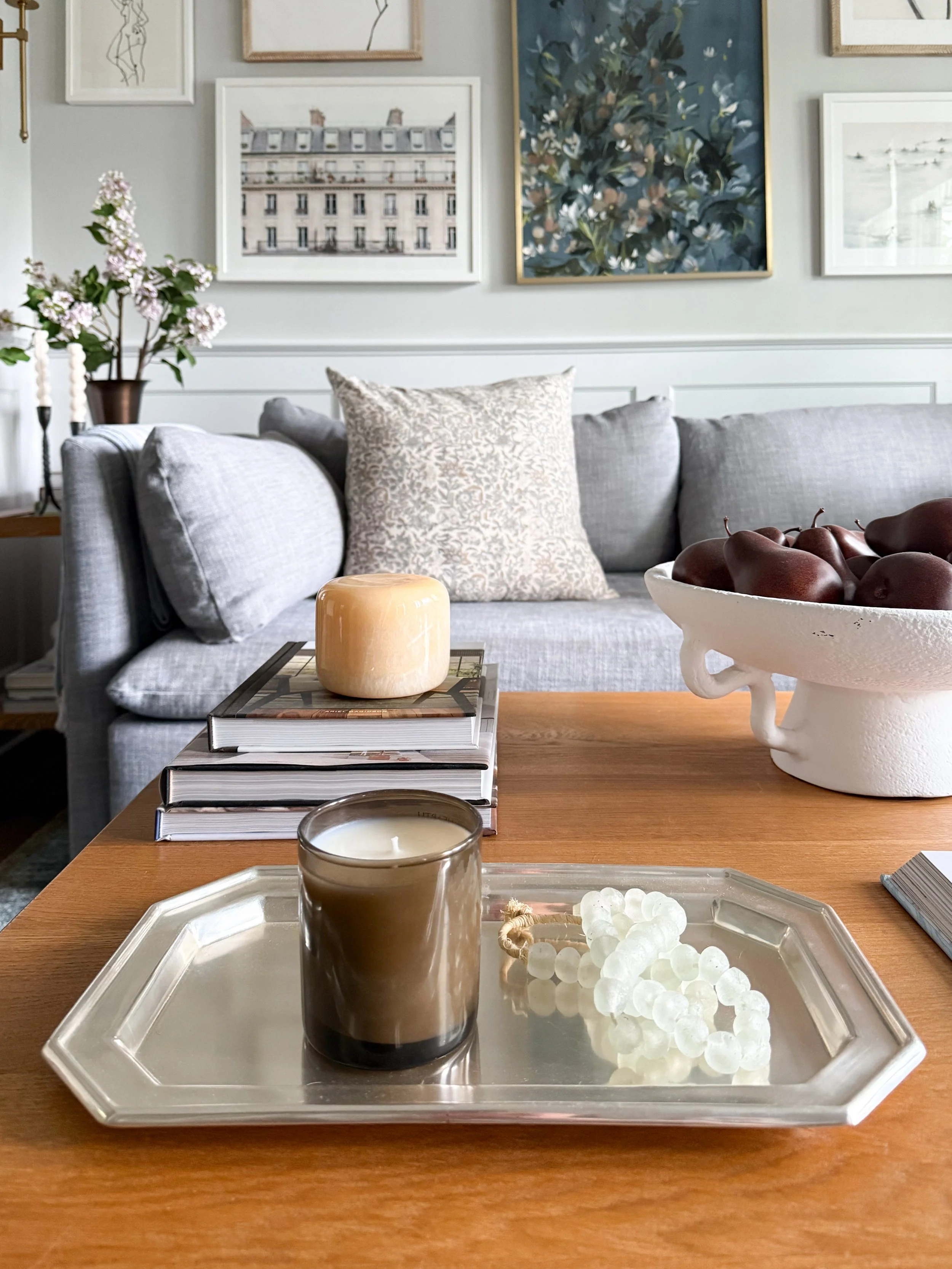 Neutral marble table lamp with linen shade styled on black cabinet beside window in soft coastal inspired home with layered textures and warm lighting