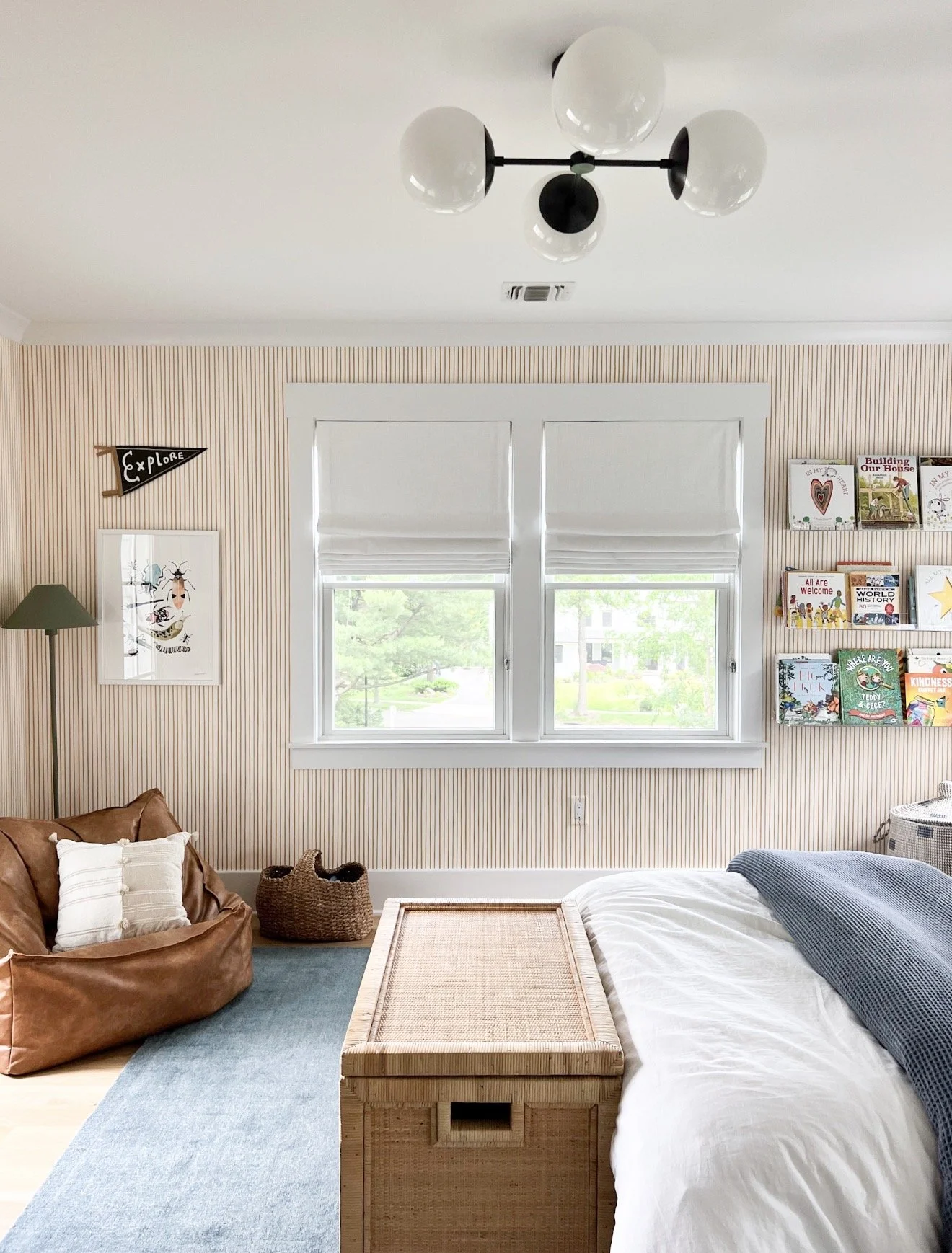 Children's bedroom with striped wallpaper, black and white globe ceiling light, leather bean bag chair, and blue area rug.