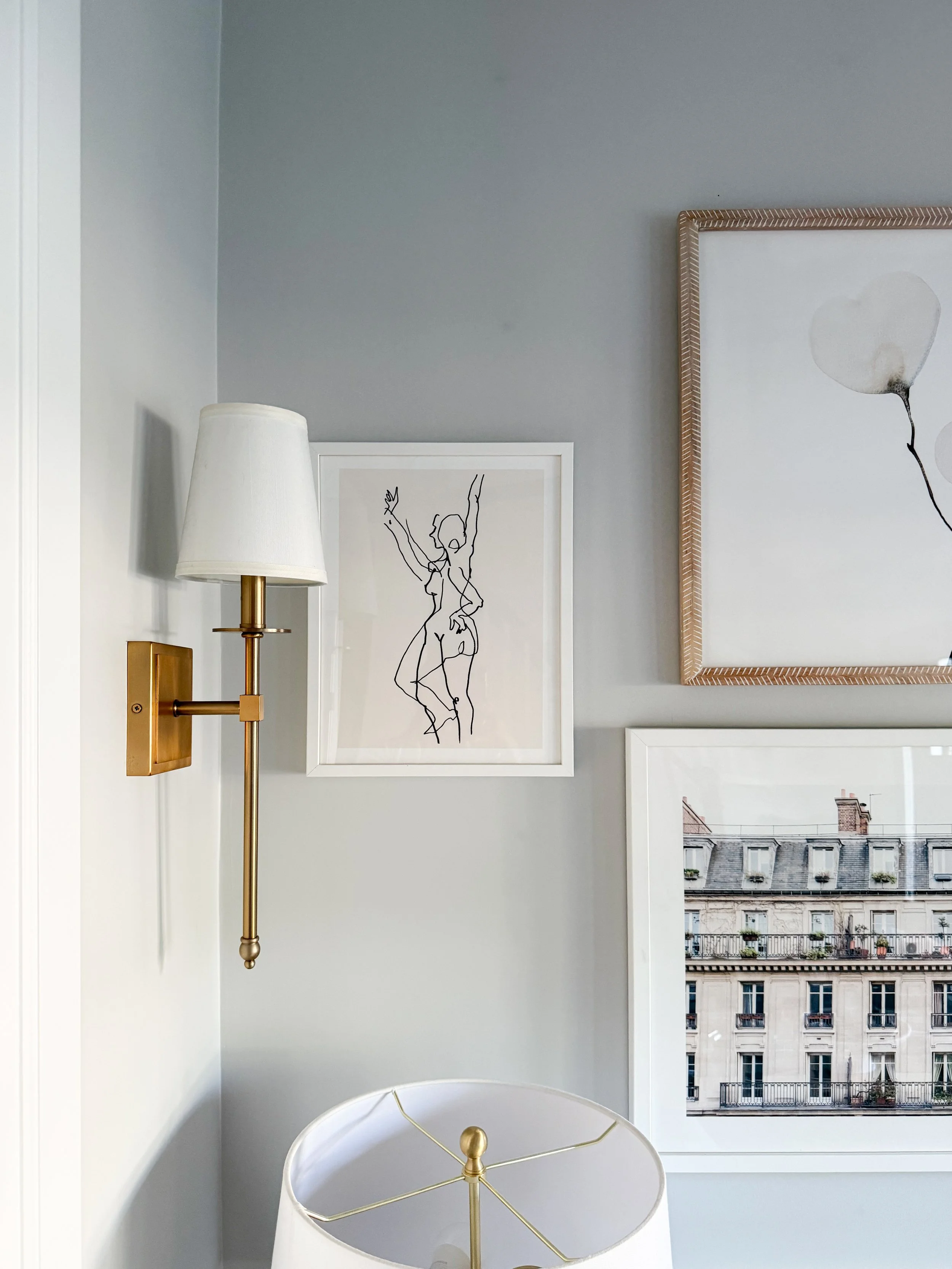 Styled living room corner featuring framed artwork, a table lamp, decorative accessories, and layered textures for a collected designer look.