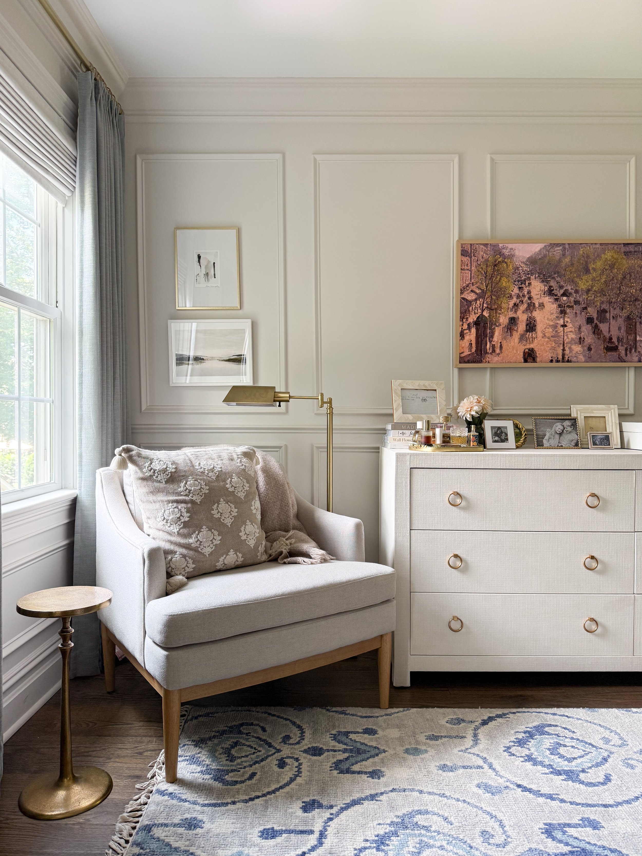 Cozy bedroom reading nook with a neutral accent chair, floor lamp, side table, layered textiles, and framed artwork.