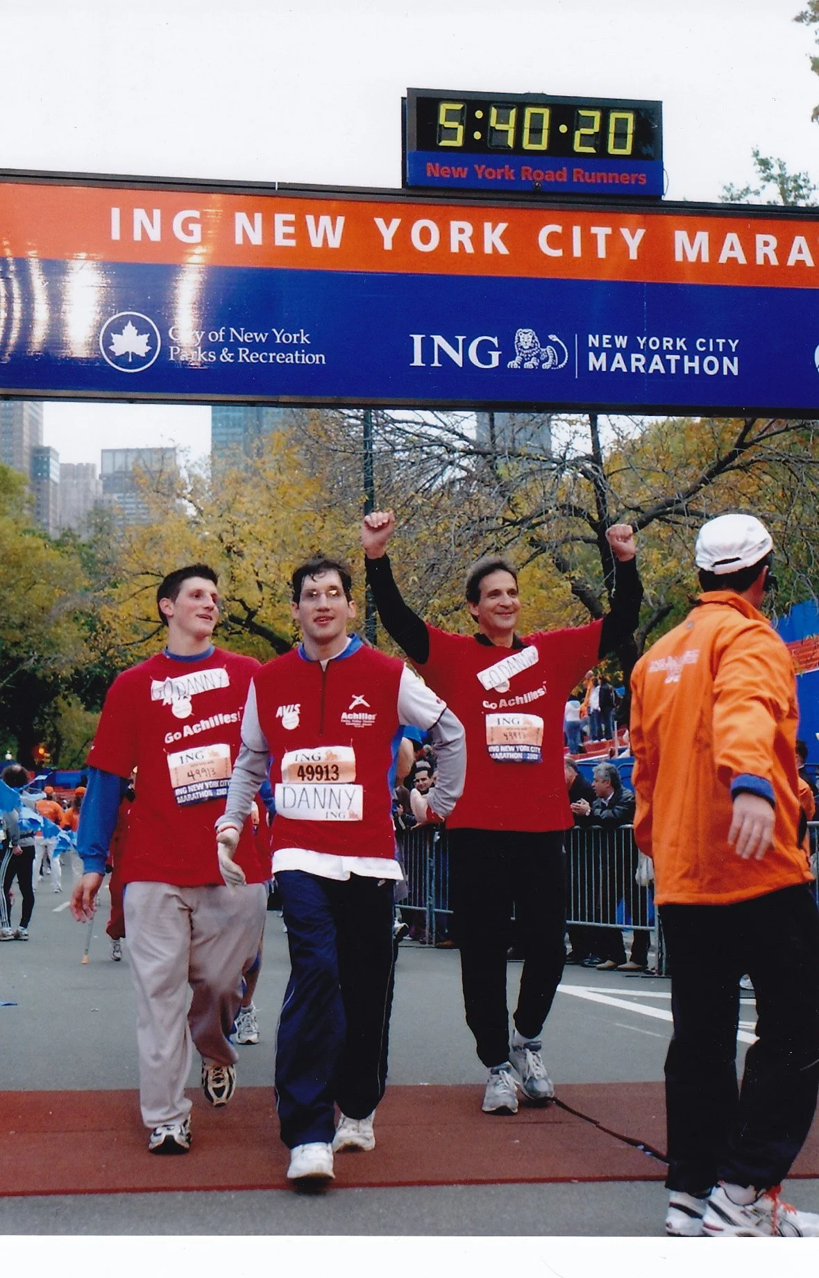  Image of Daniel, his father Ken, and his brother Michael smiling while crossing the finish line at the NYC Marathon. 