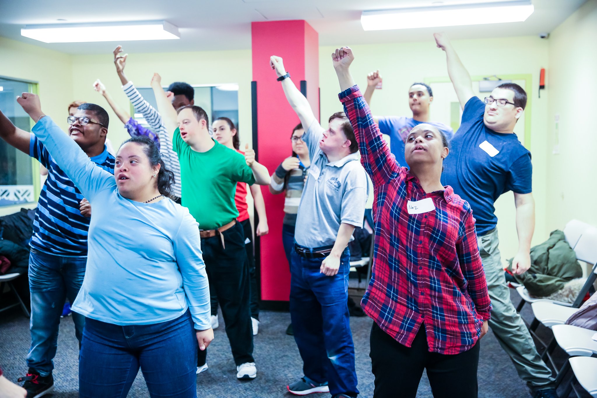  Image of a movement class at the DMF music center, featuring the participants raising their right arms up in the air. 