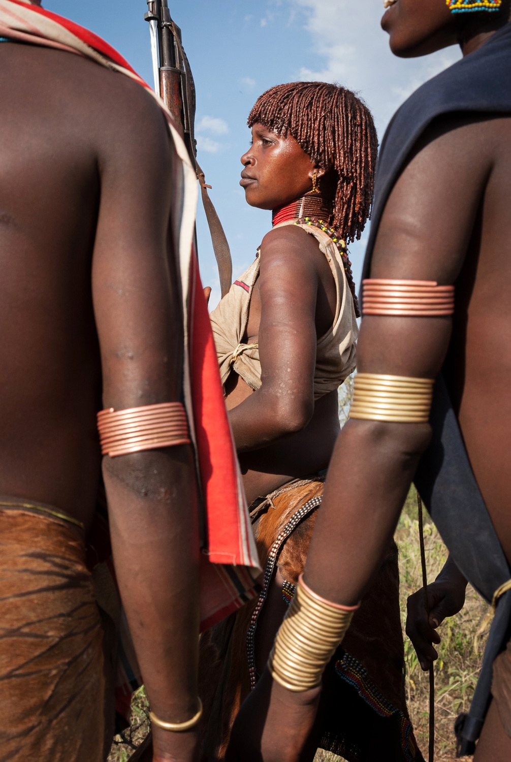  A Hamar woman dances holding a gun as her brother prepares to leap across the cattle; Omo Valley, Ethiopia 