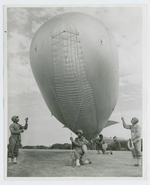 Four men from a black barrage balloon unit hoist aloft a balloon during a 1942 demonstration in Washington, D.C. Elasticized ropes allowed the envelope to expand as the balloon went up and the gas inside expanded. Photographer: Roger Smith; Photographs and Prints Division, Schomburg Center for Research in Black Culture, the New York Public Library, Astor, Lenox and Tilden Foundations