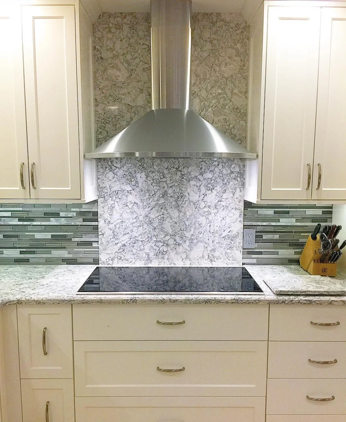 Cambria berwyn quartz countertops and backsplash with induction range cooktop and stainless steel range door. frameless white shaker cabinets
