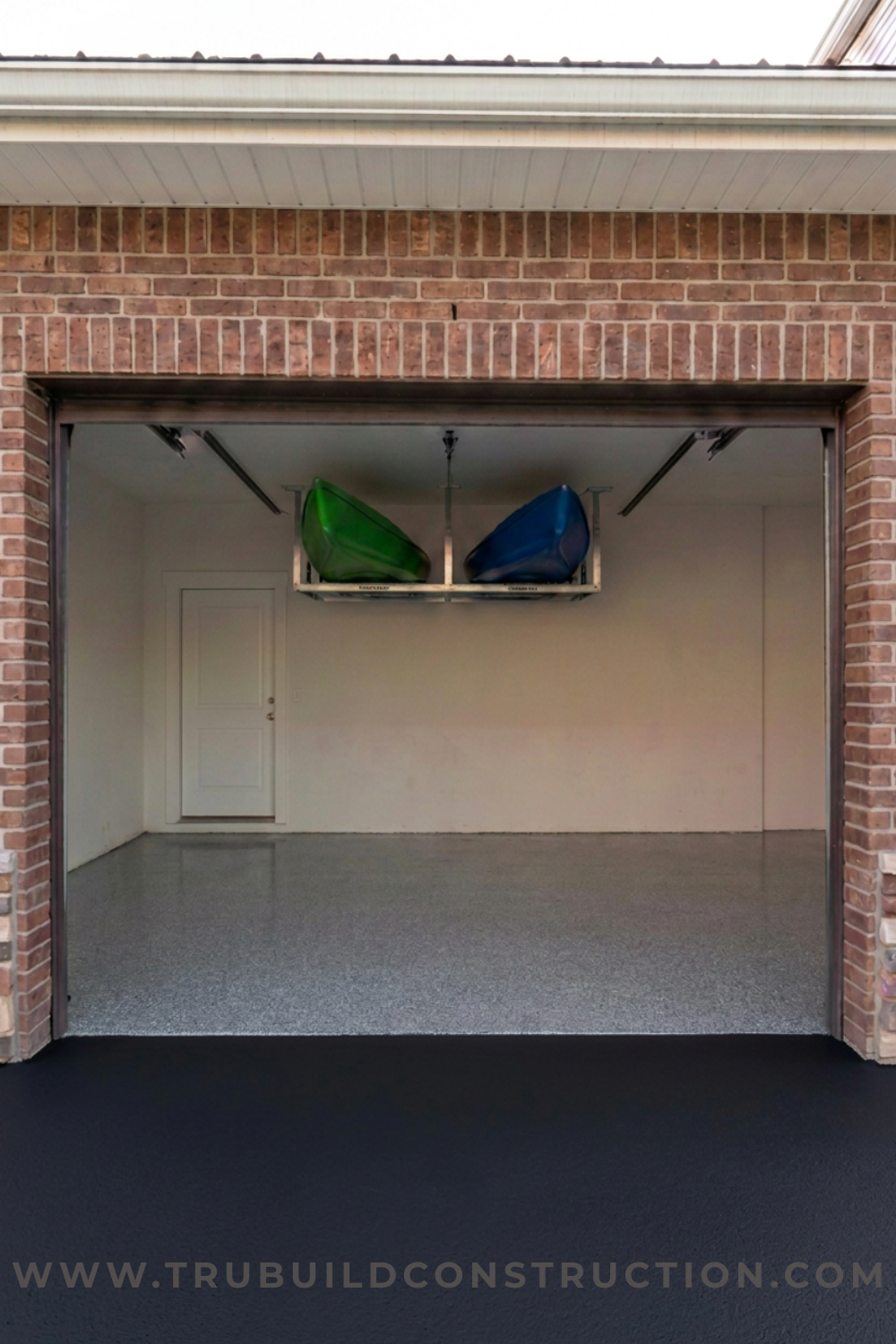 Two kayaks stored on an overhead rack near the ceiling of a garage, demonstrating a space-saving solution for large outdoor equipment.