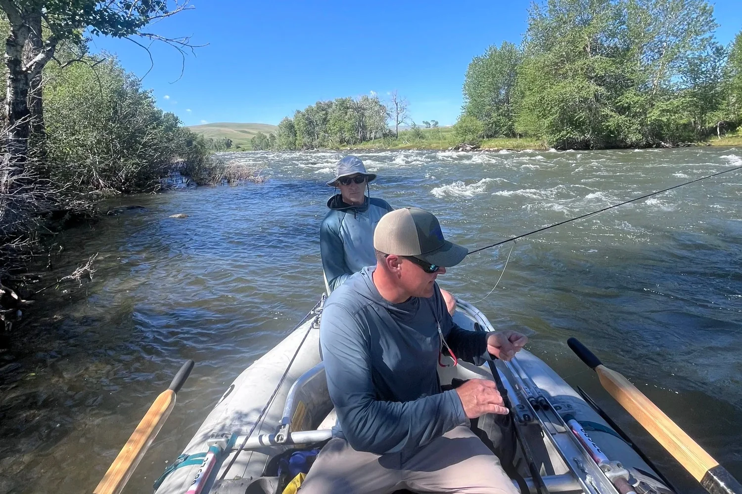 Angler fishing from a raft on fast freestone water, typical of the Boulder or Stillwater rivers in Montana.