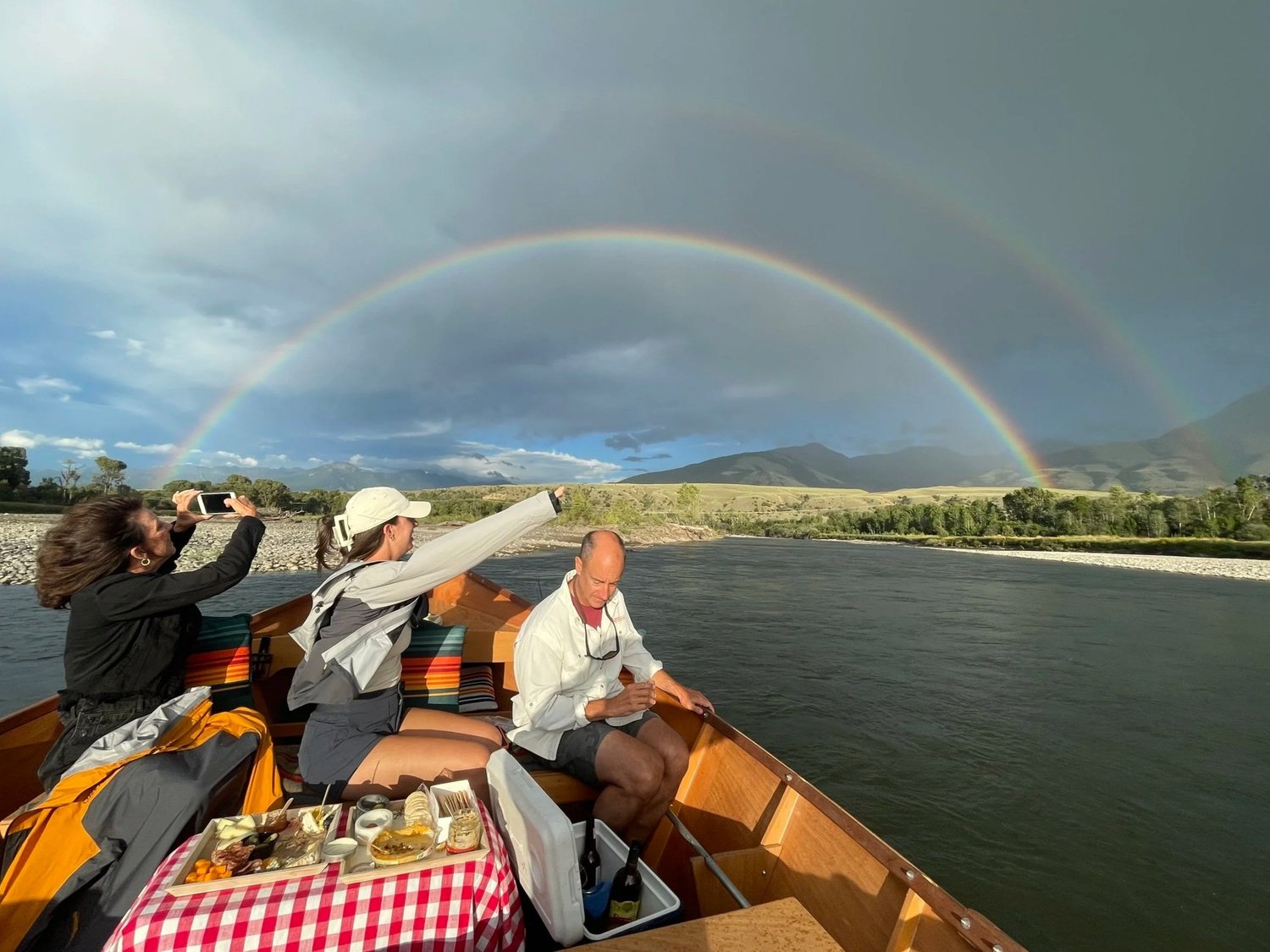 Wooden boat tour on the Yellowstone River in Paradise Valley, Montana with guests under a rainbow