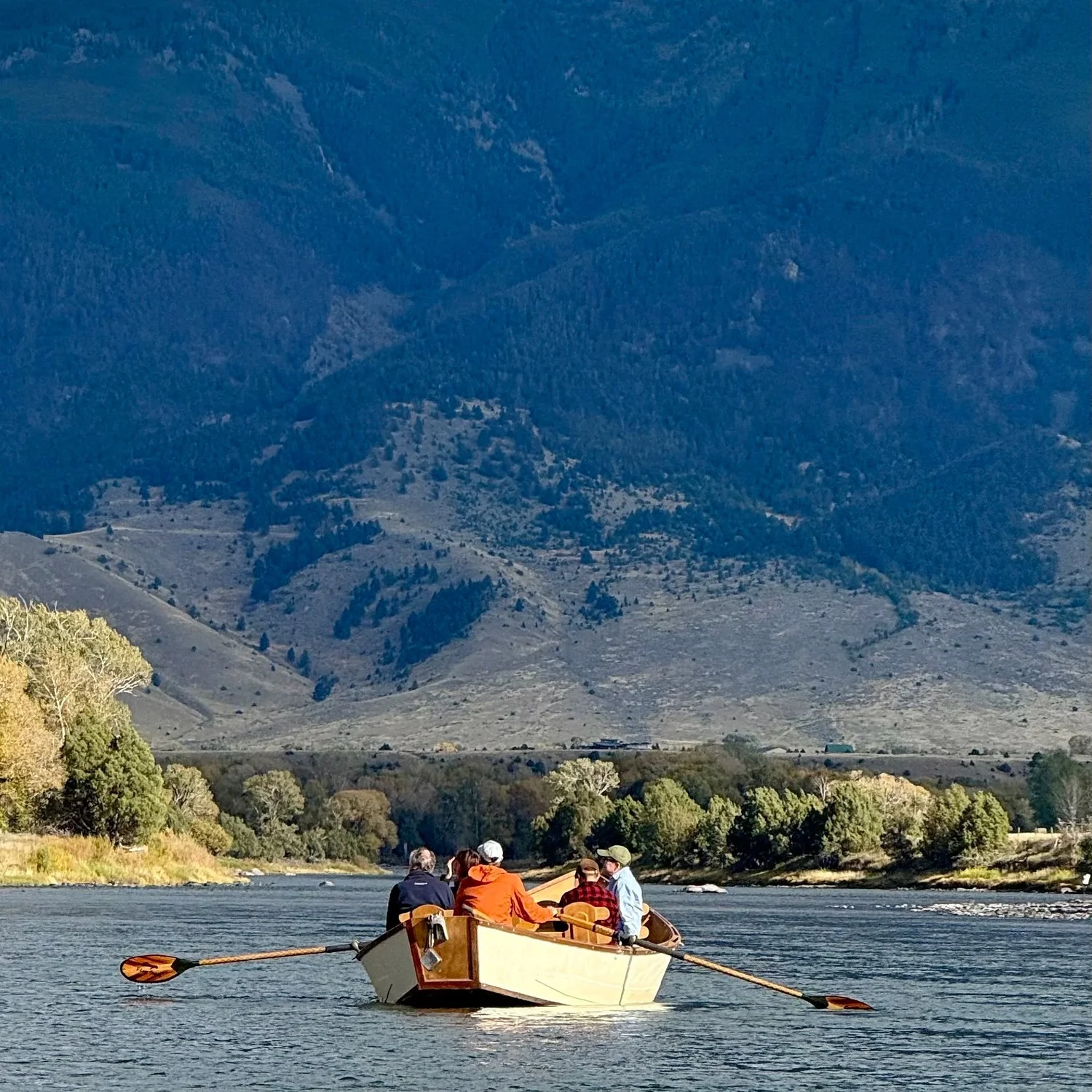 Guests relaxing in a traditional wooden boat on the Yellowstone River in Paradise Valley Montana.