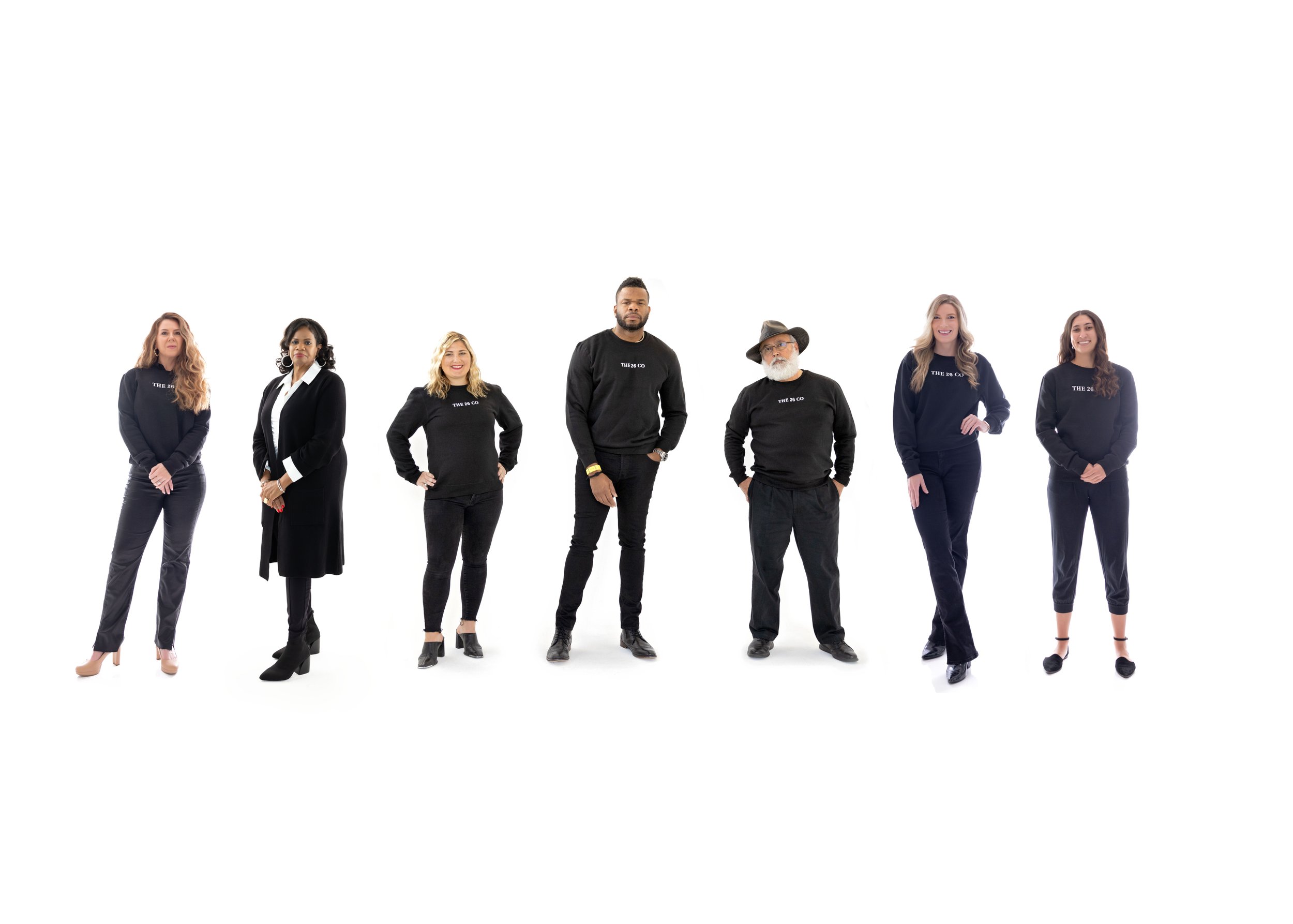 Seven diverse individuals standing in a line against a white background, dressed in black clothing.