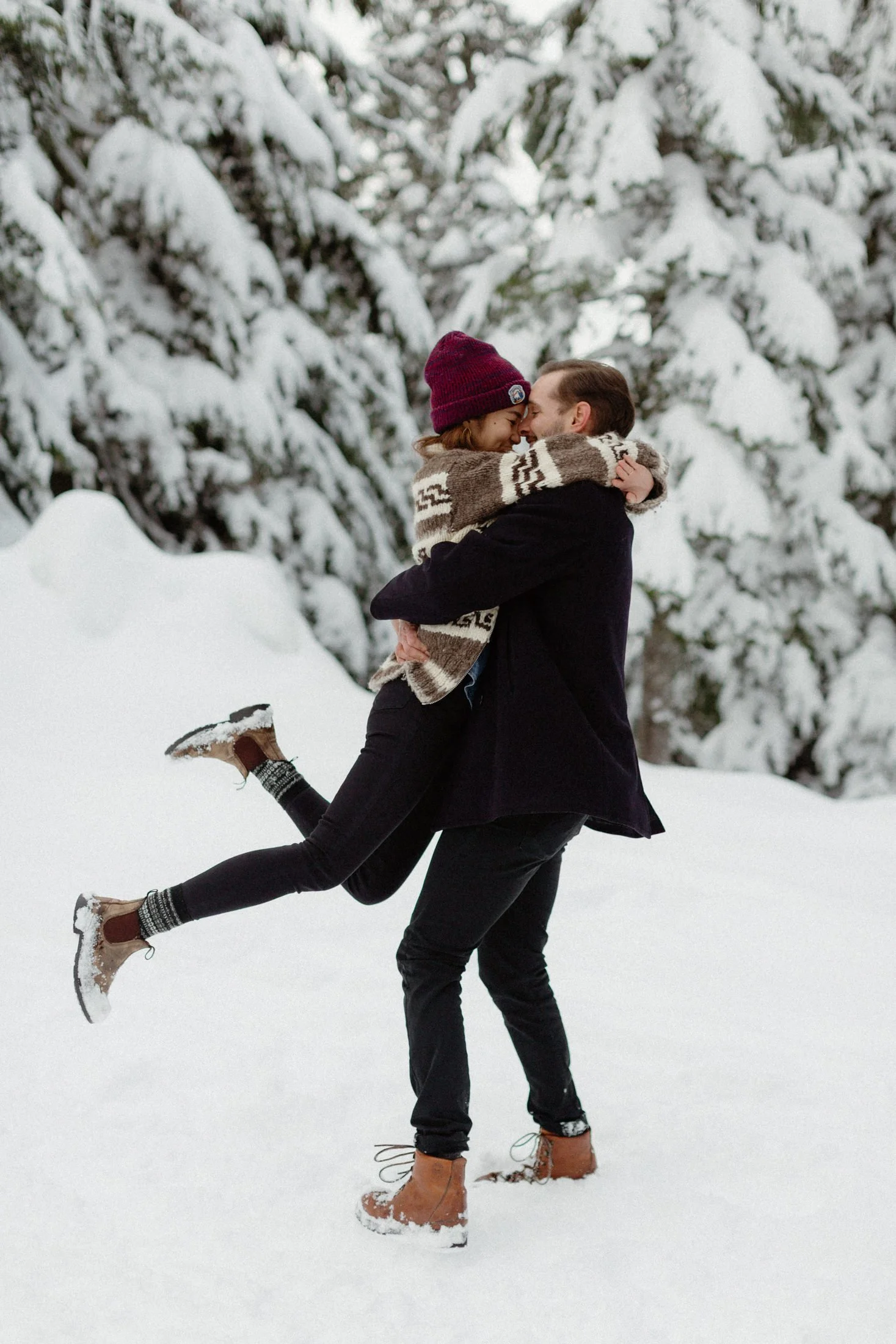a man spins his fiance around with her legs kicked up in a winter wonderland setting in the forest of grouse mountain