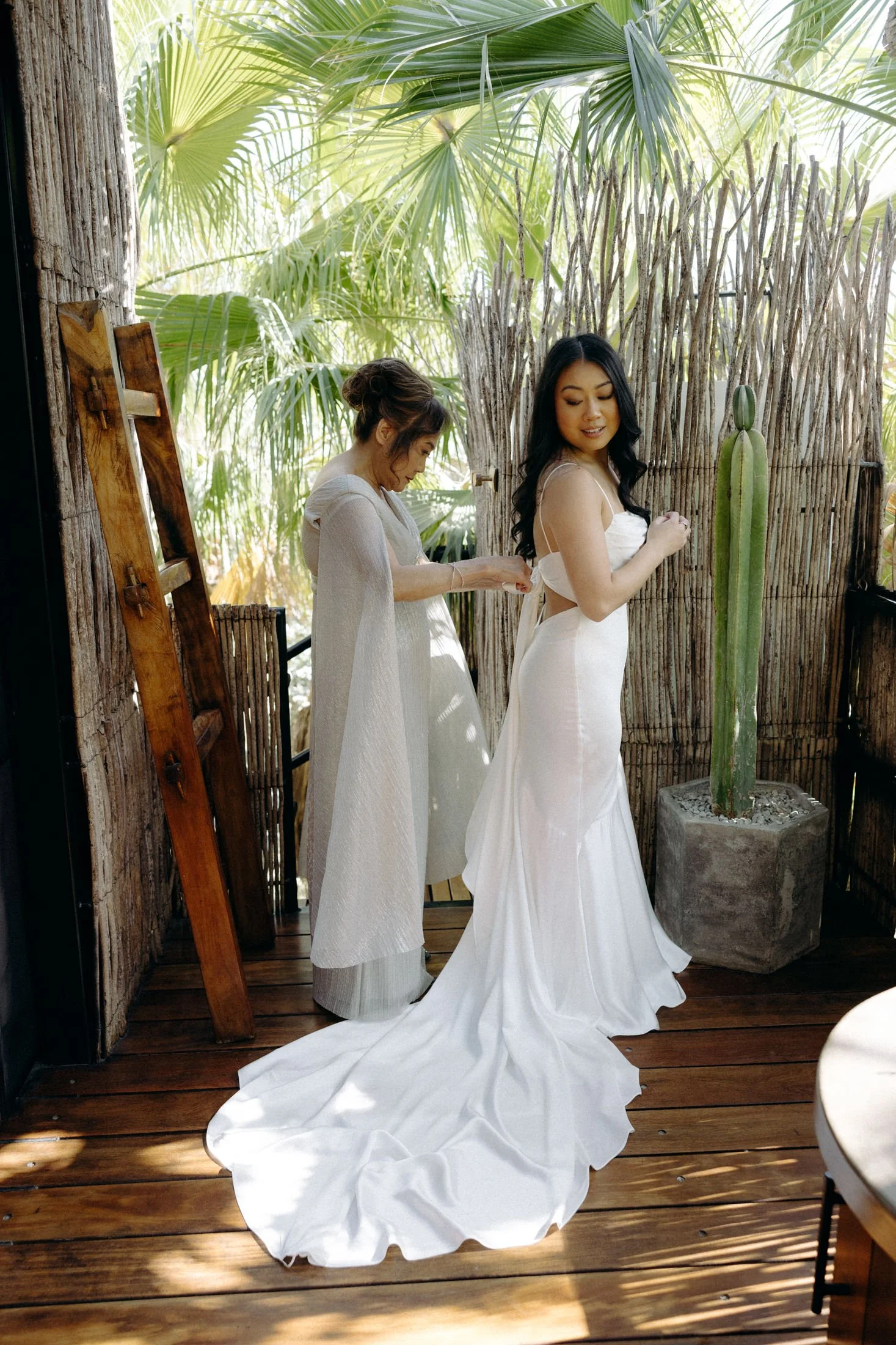 A bride and her mother putting on her wedding dress on the balcony of one of the treehouses that are covered in bamboo at the acre resort in Los Cabos, Mexico