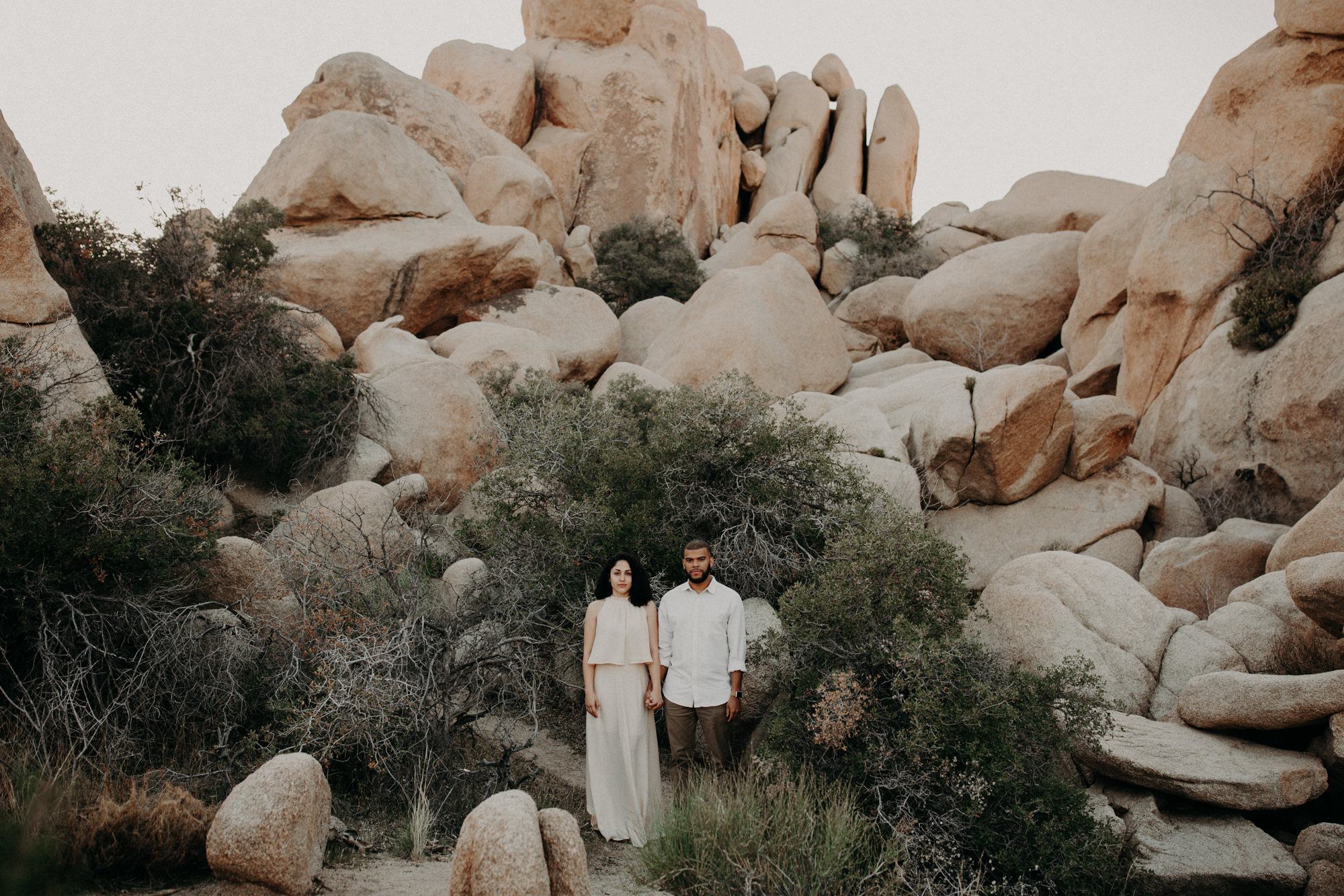 An engaged couple holding hands, perfectly centred in the boulders of Joshua Tree Park.